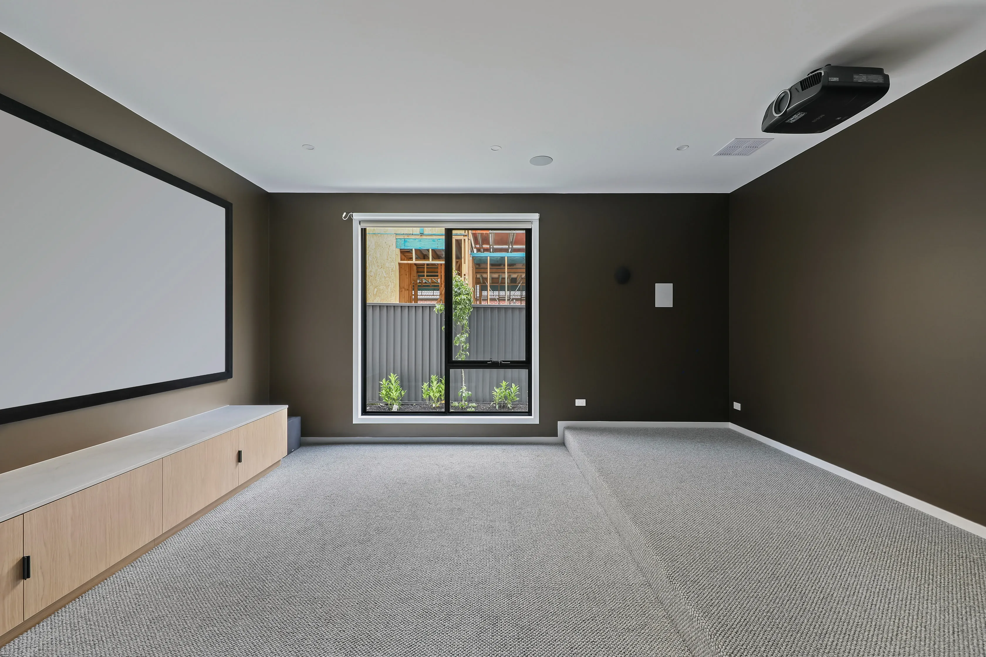 Carpeted home theatre room at Mount Waverley Residence with a projector screen, ceiling projector and built-in oak cabinetry