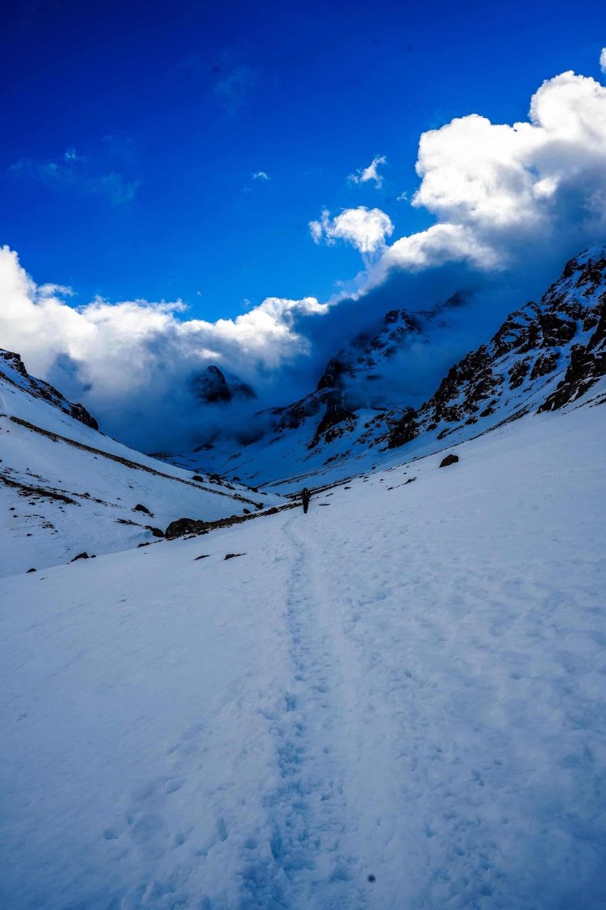 man in blue jacket and black pants standing on snow covered mountain under blue sky during