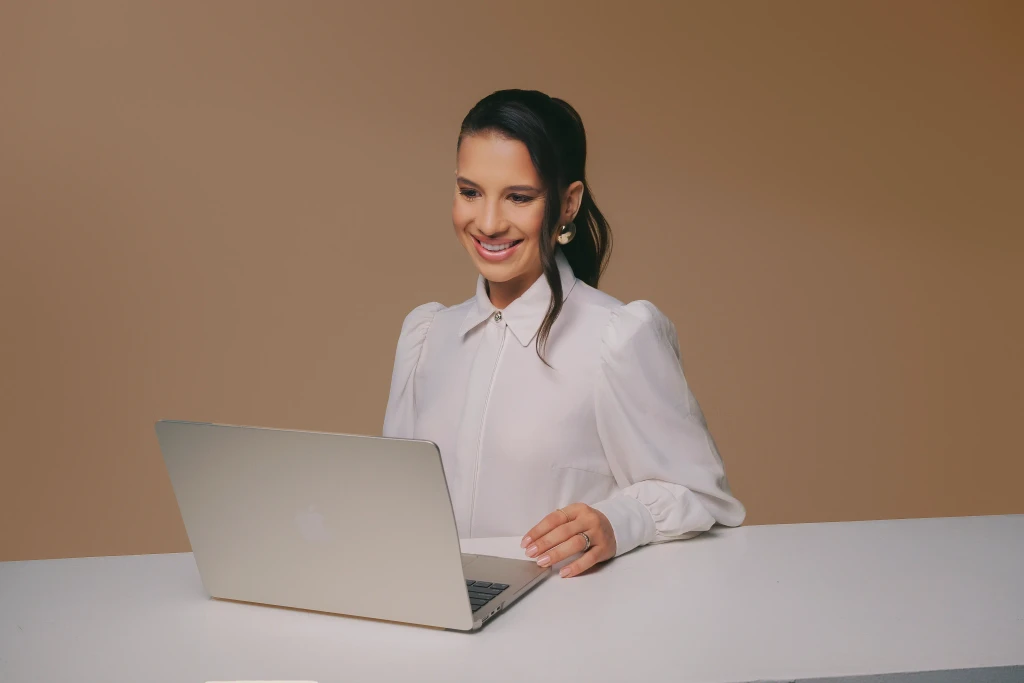 Isabela Ramos sorrindo em frente ao notebook com blusa branca – foto profissional estúdio