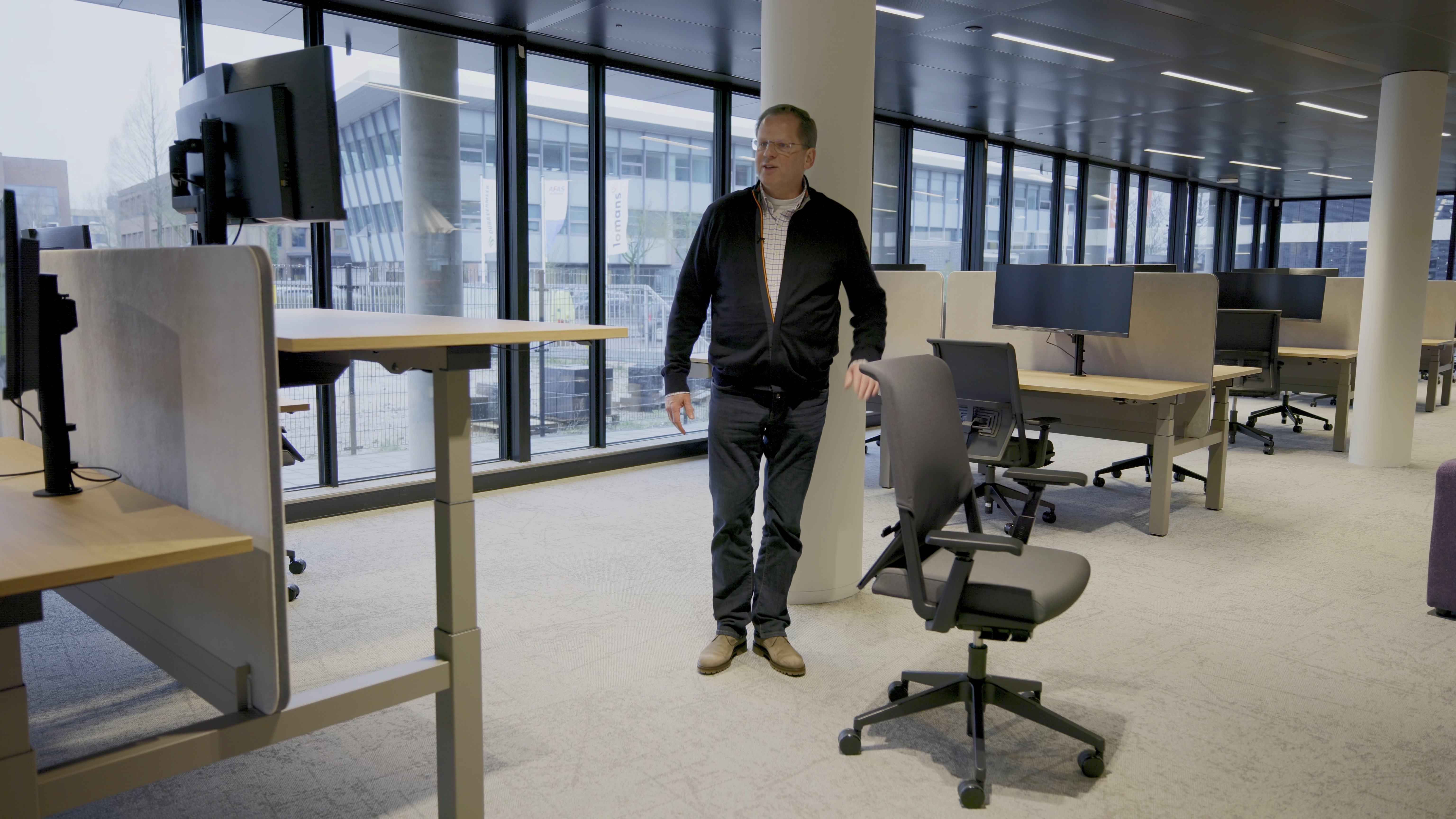 Gerard van DSN Workspace Solutions loopt door een open kantoorruimte met in hoogte verstelbare bureaus en bureaustoelen in AFAS DotNL, Leusden