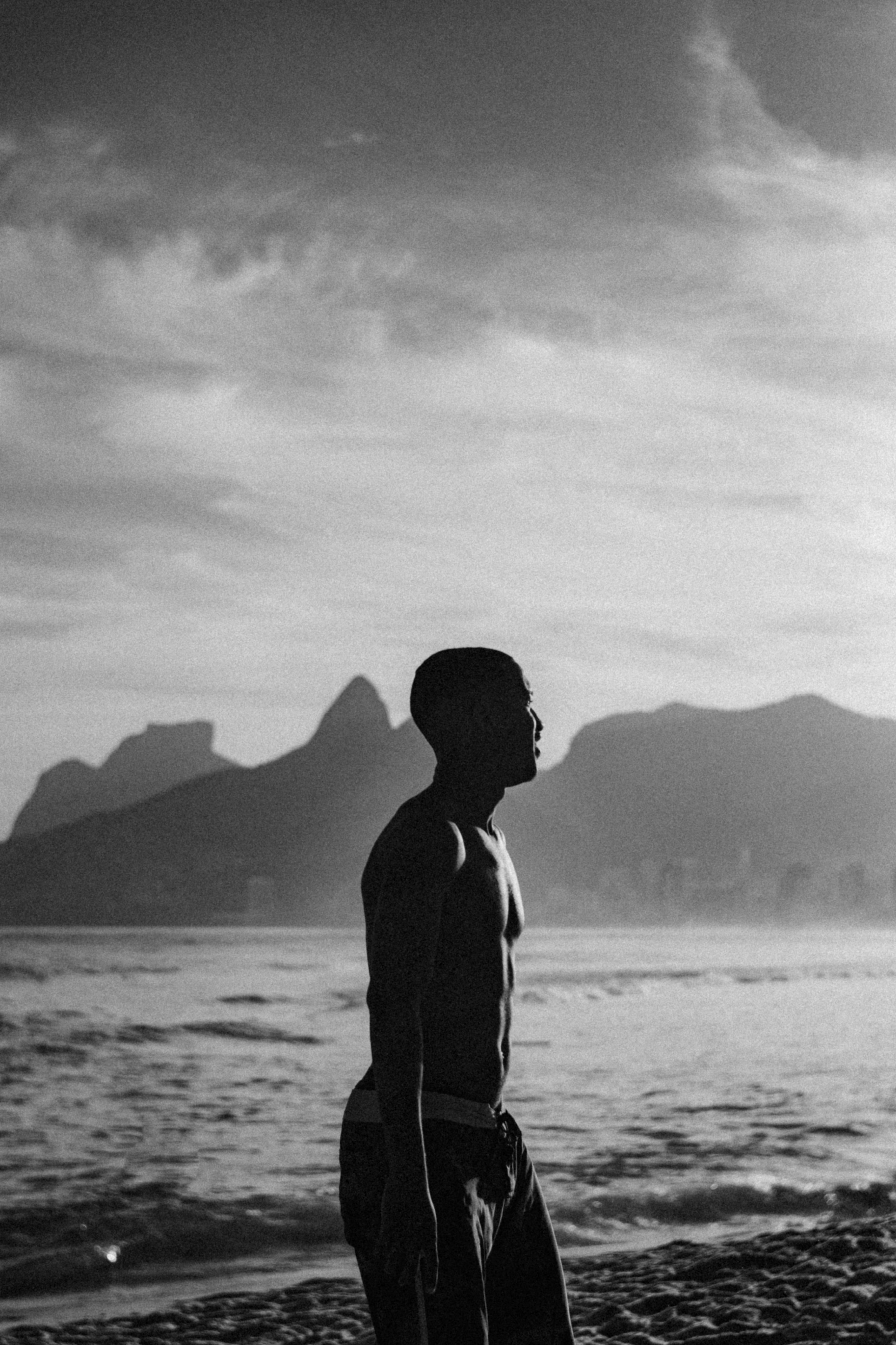 A black and white photo of a man standing on the beach.