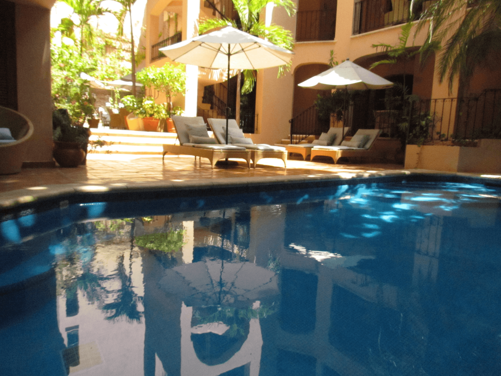 Outdoor courtyard pool with lounge chairs and umbrellas at Acanto Hotel Playa del Carmen.
