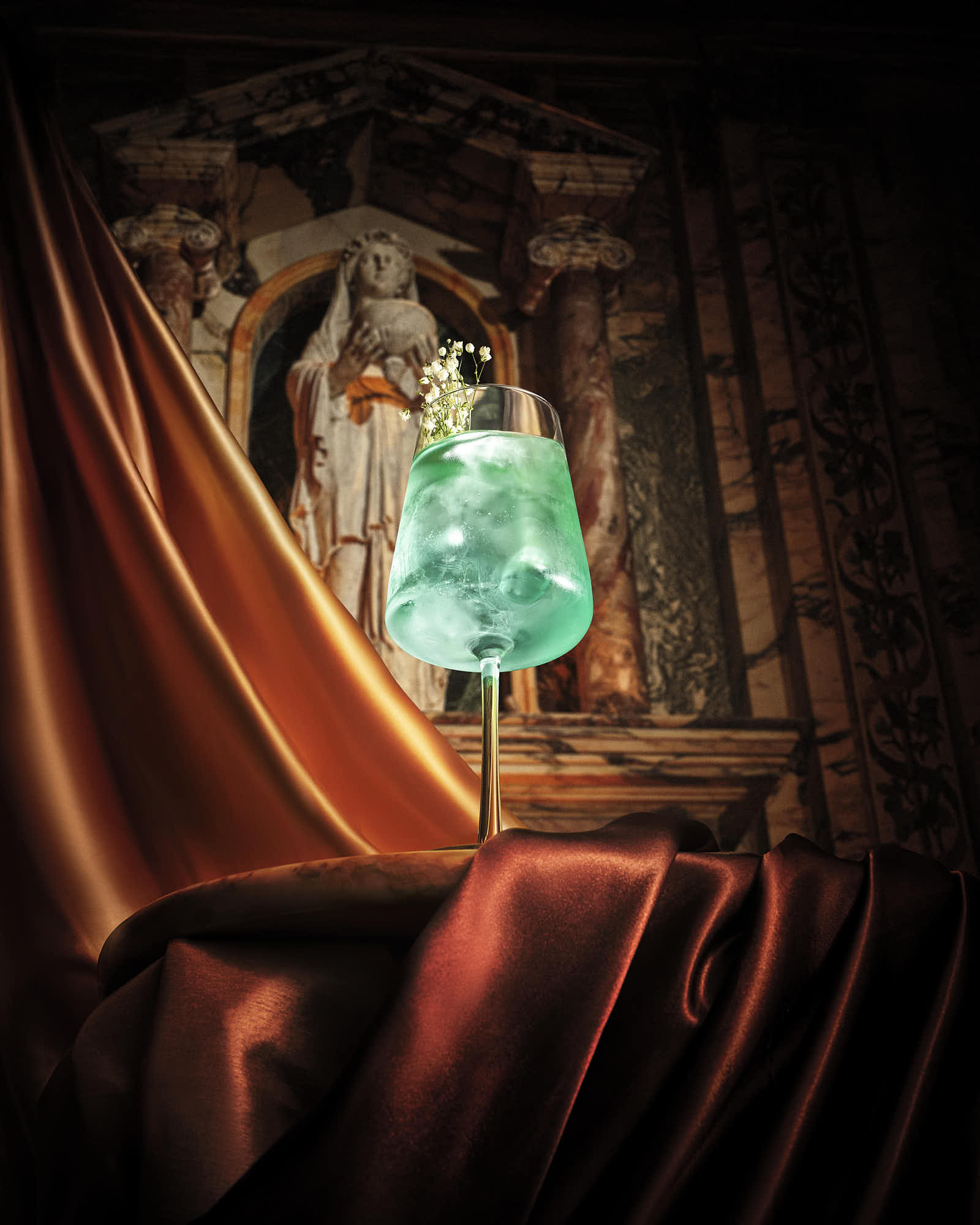 A glowing green cocktail displayed on an ornate marble background, partially draped in rich red fabric.