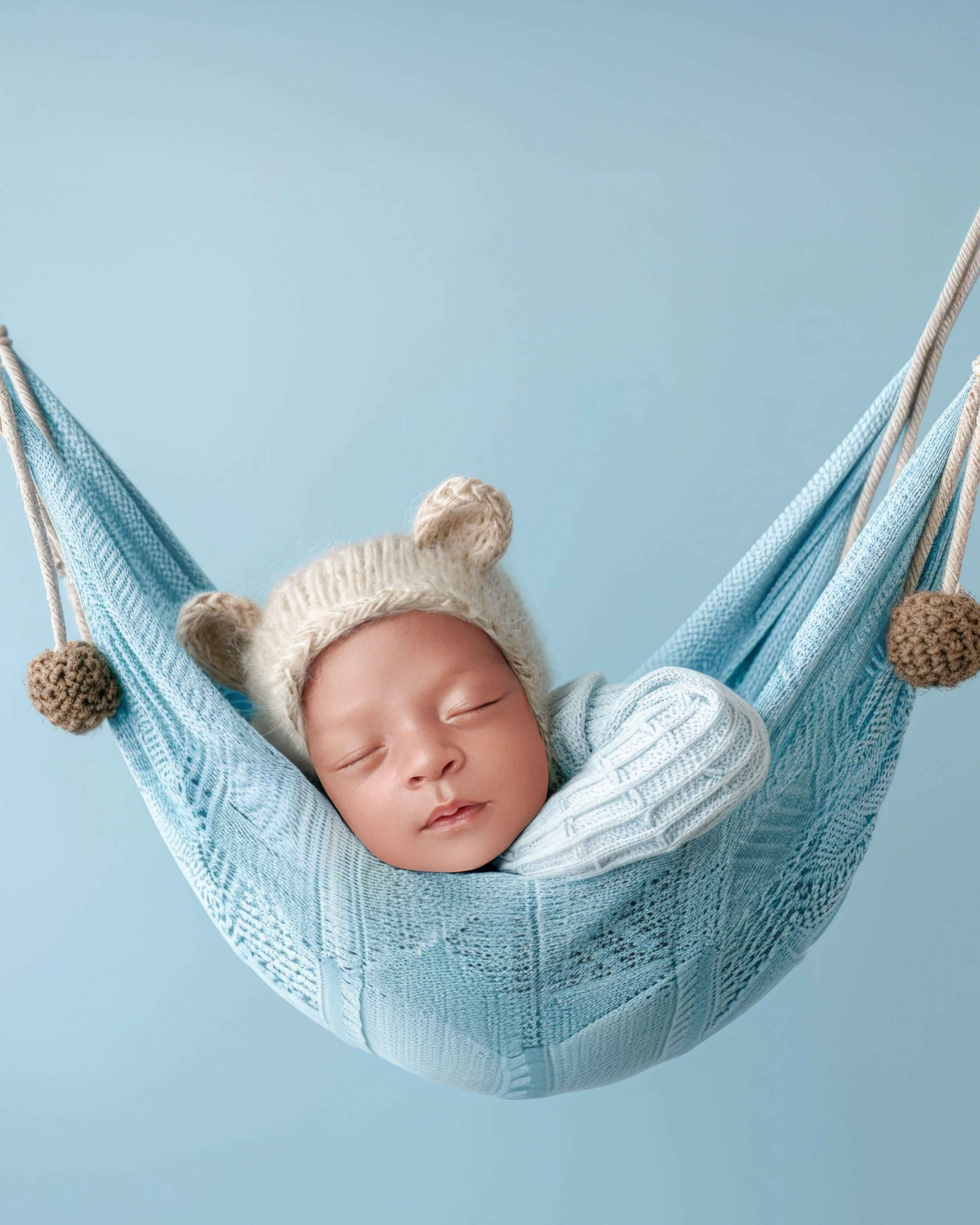 Newborn baby boy sleeping in soft blue hammock pose during studio newborn session