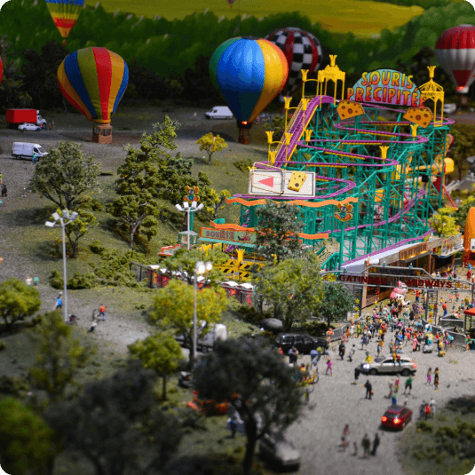 A vibrant close-up photograph of a miniature village adorned with festive Christmas lights, highlighting the detailed craftsmanship of the exhibit