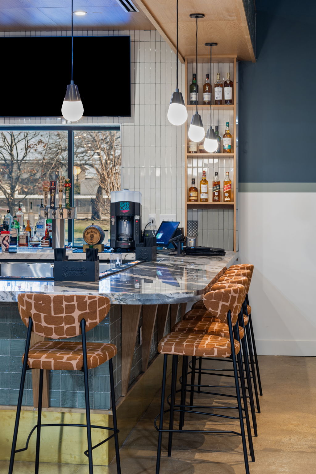 Close-up of At Fault bar interior featuring frontlit signage, tiled bar front, pendant lighting, and seating within the Dallas pickleball venue.