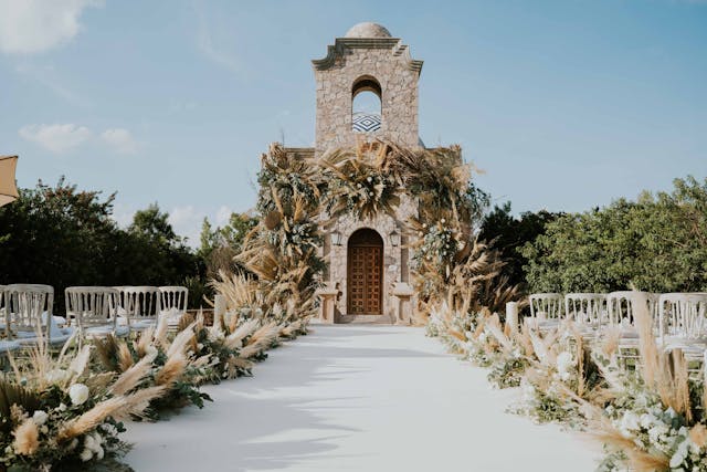 A serene outdoor wedding setup with white chairs arranged on green grass under a canopy of trees.