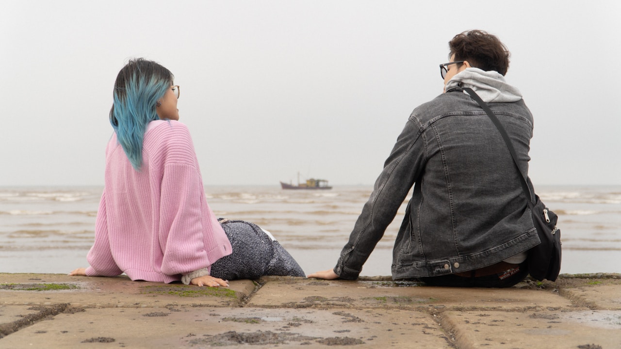 Couple sitting apart on a pier with emotional distance between them, representing relationship uncertainty | Photo by Tung Hoang on Unsplash