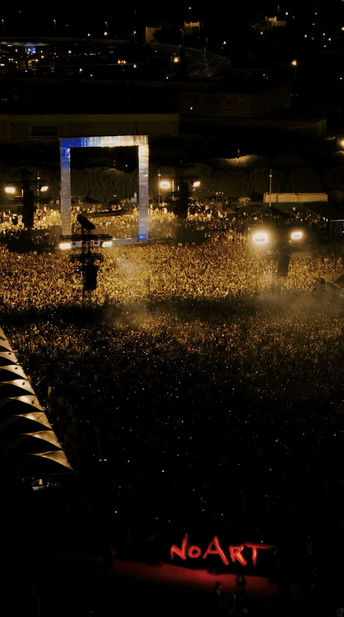 Close-up portrait of a person wearing a gray insulated hooded jacket with the hood up, showing their face framed by the hood against a light background.