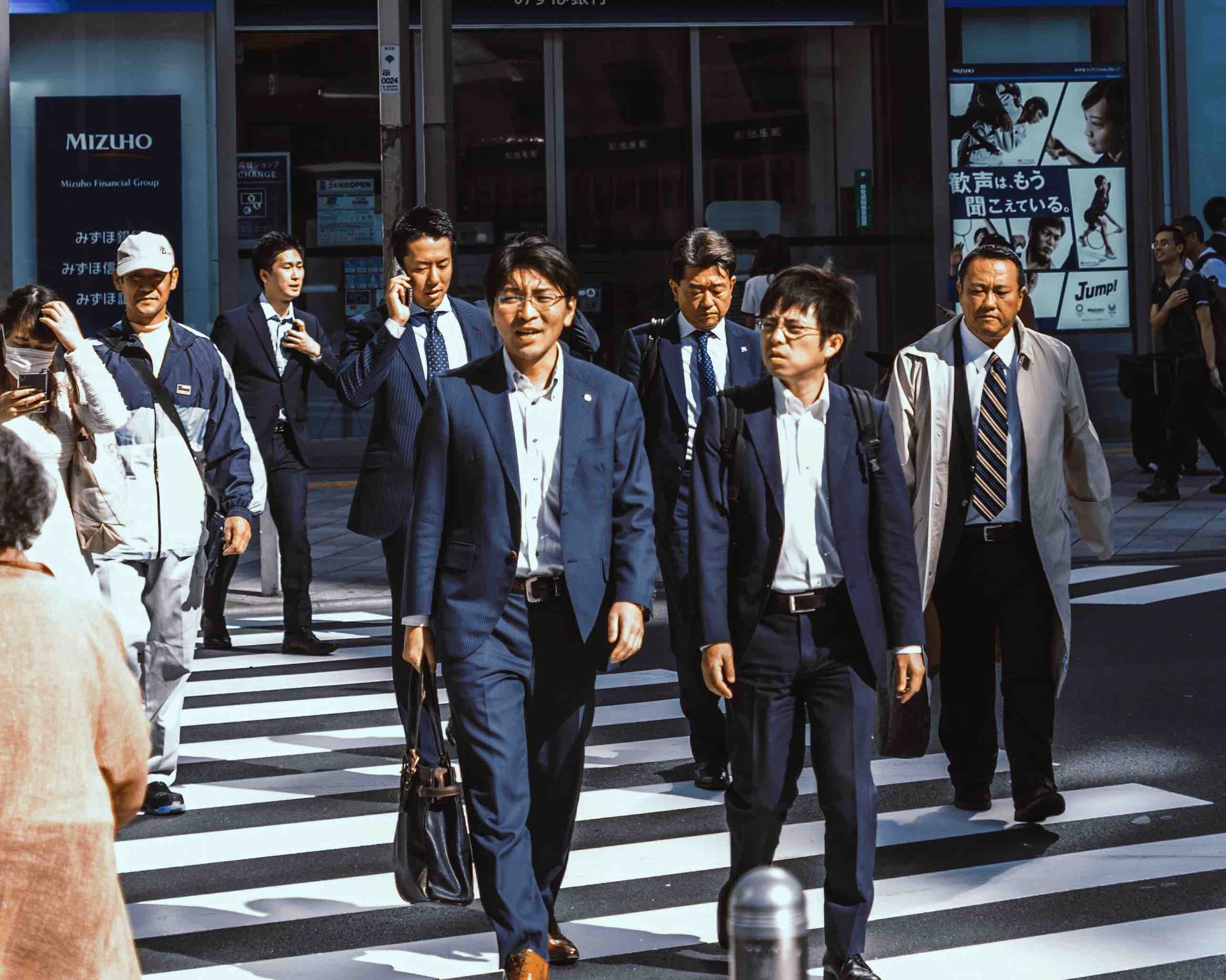 Japanese business men walking across the street in Tokyo side by side.