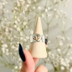 צילום תקריב של טבעת כסף עם חיתוך פרח לוטוס על מעמד עץ, צילום מוצר מקצועי של הצלמתShiriz שירי עציץ על רקע פרחים לבנים עדינים.