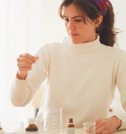 Uma mulher com roupas brancas utiliza um conta gotas para gerar essências naturais.