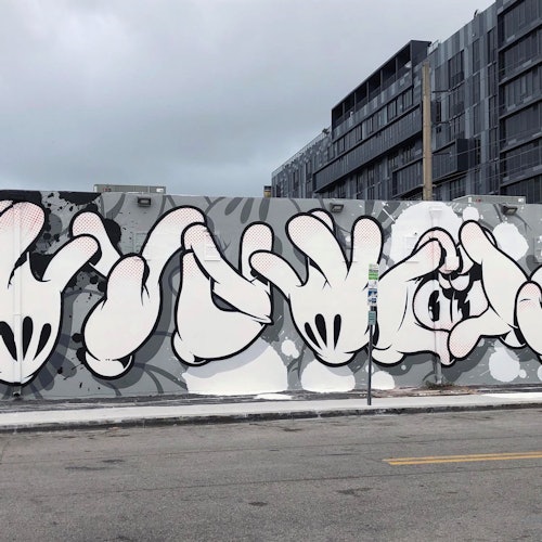 墙上的涂鸦描绘了一系列风格化的卡通手部姿势，背景是一座灰色建筑。