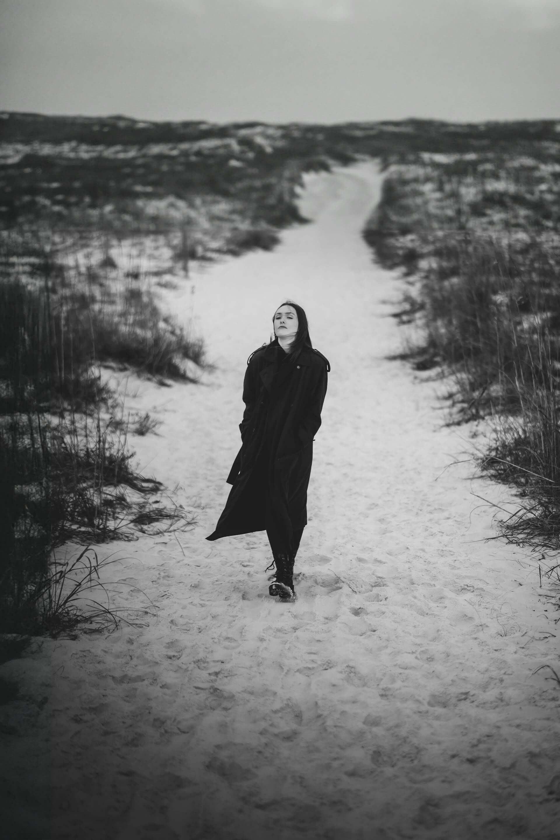 A woman in a black coat strolls along a snowy path, surrounded by a serene winter landscape