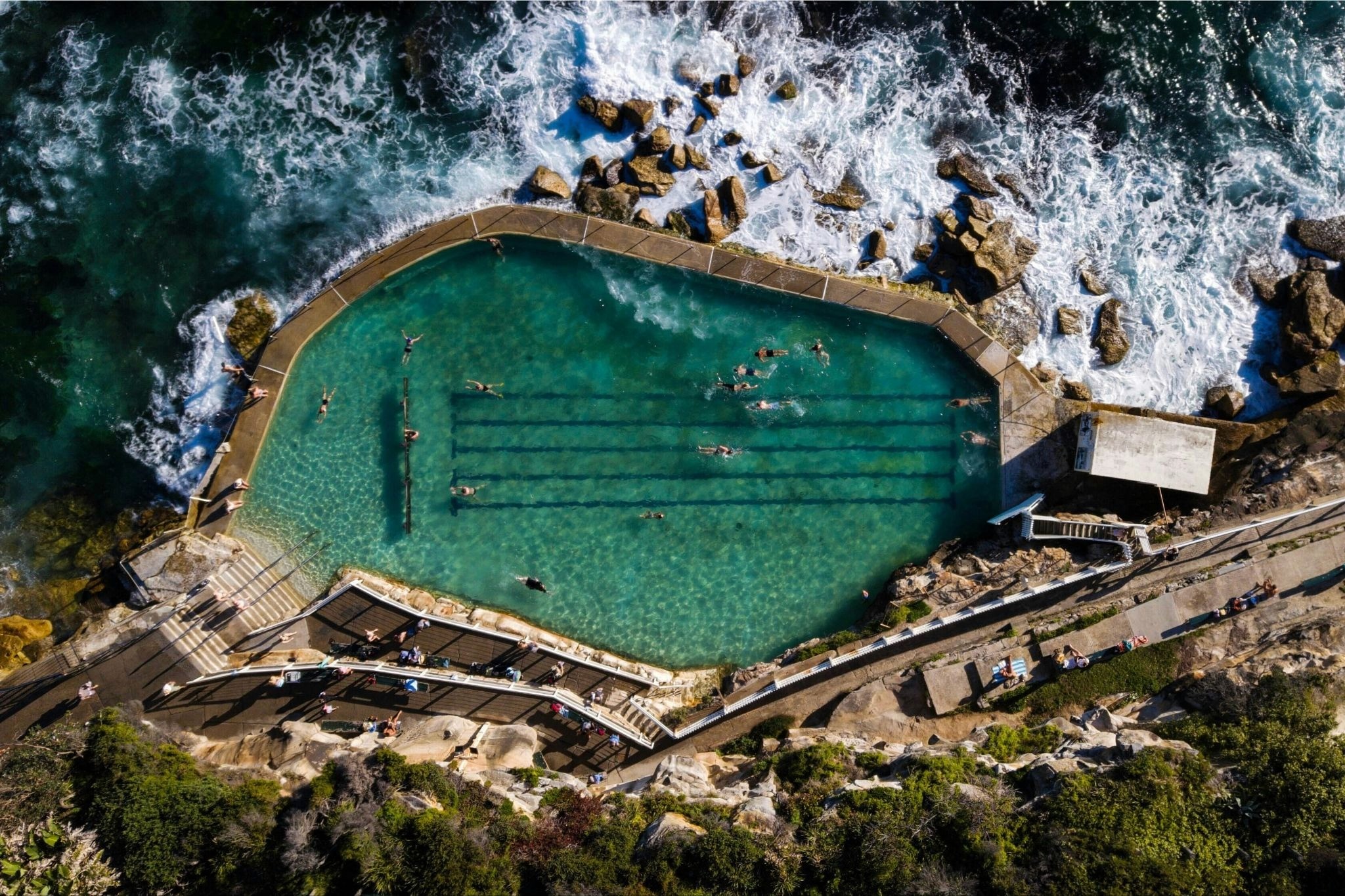 Overhead shot of a turquoise irregular pool with waves crashing alongside it, Bronte Baths in Sydney