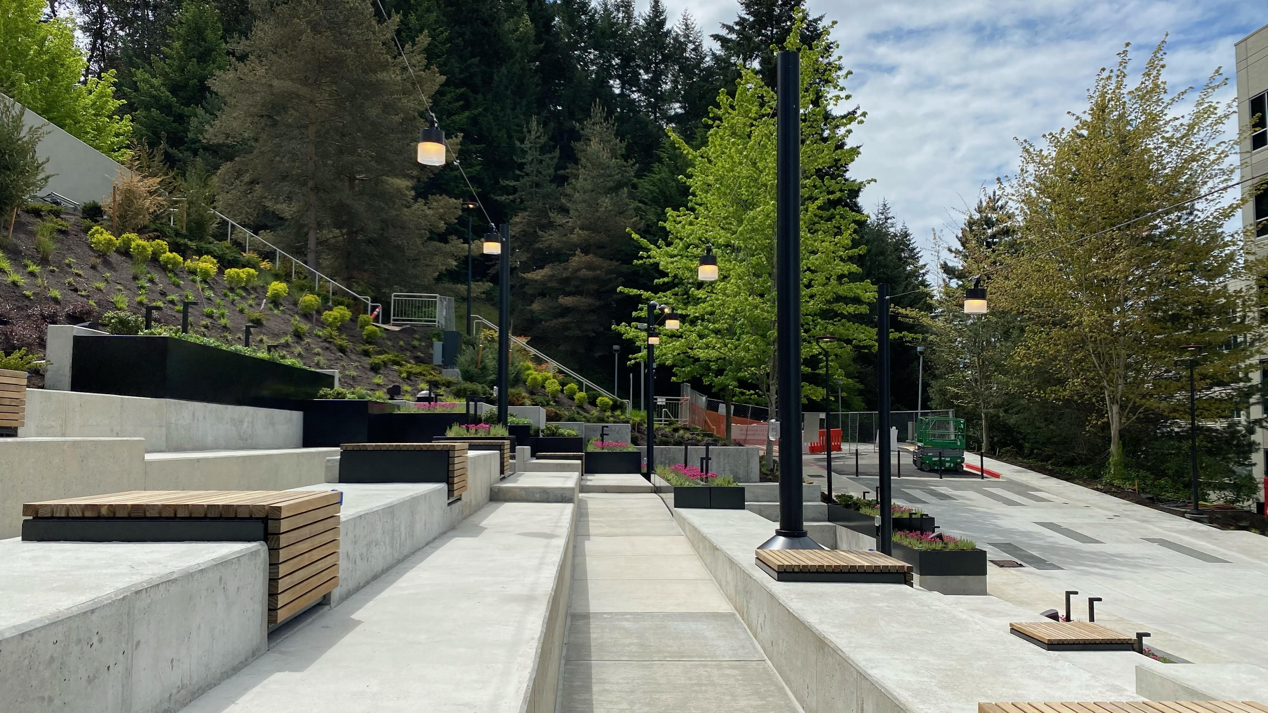 A wooden bench set along the concrete tiers of the accessible amphitheater, offering a serene view of the green hillside and trees beyond.