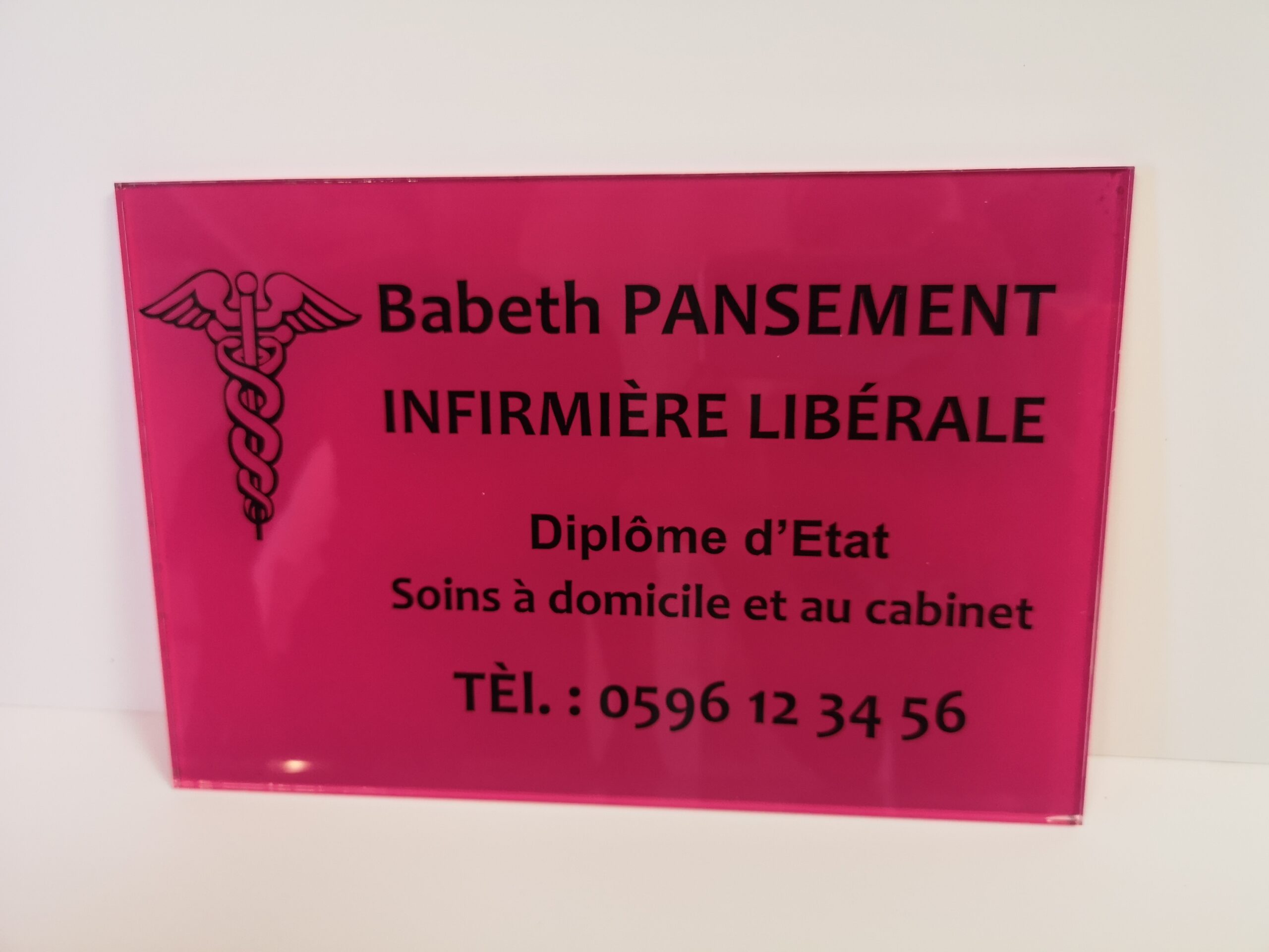 Une plaque rose vif avec un caducée médical sur la gauche. Le texte en français indique : « Babeth Pansement, Infirmière Libérale, Diplôme d'Etat, Soins à domicile et au cabinet. » Un numéro de téléphone est également affiché.