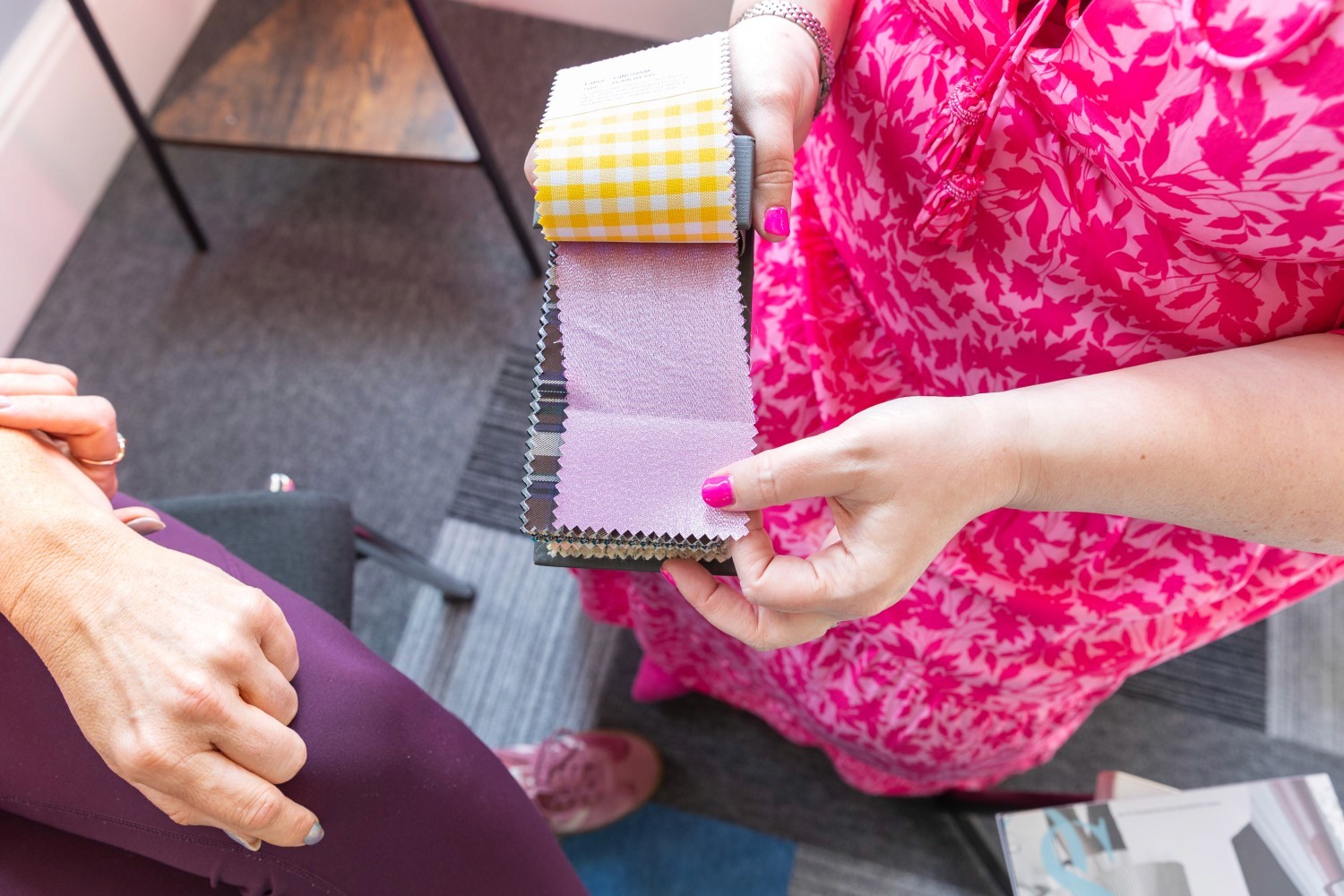 Hands presenting different fabrics in a swatch book.