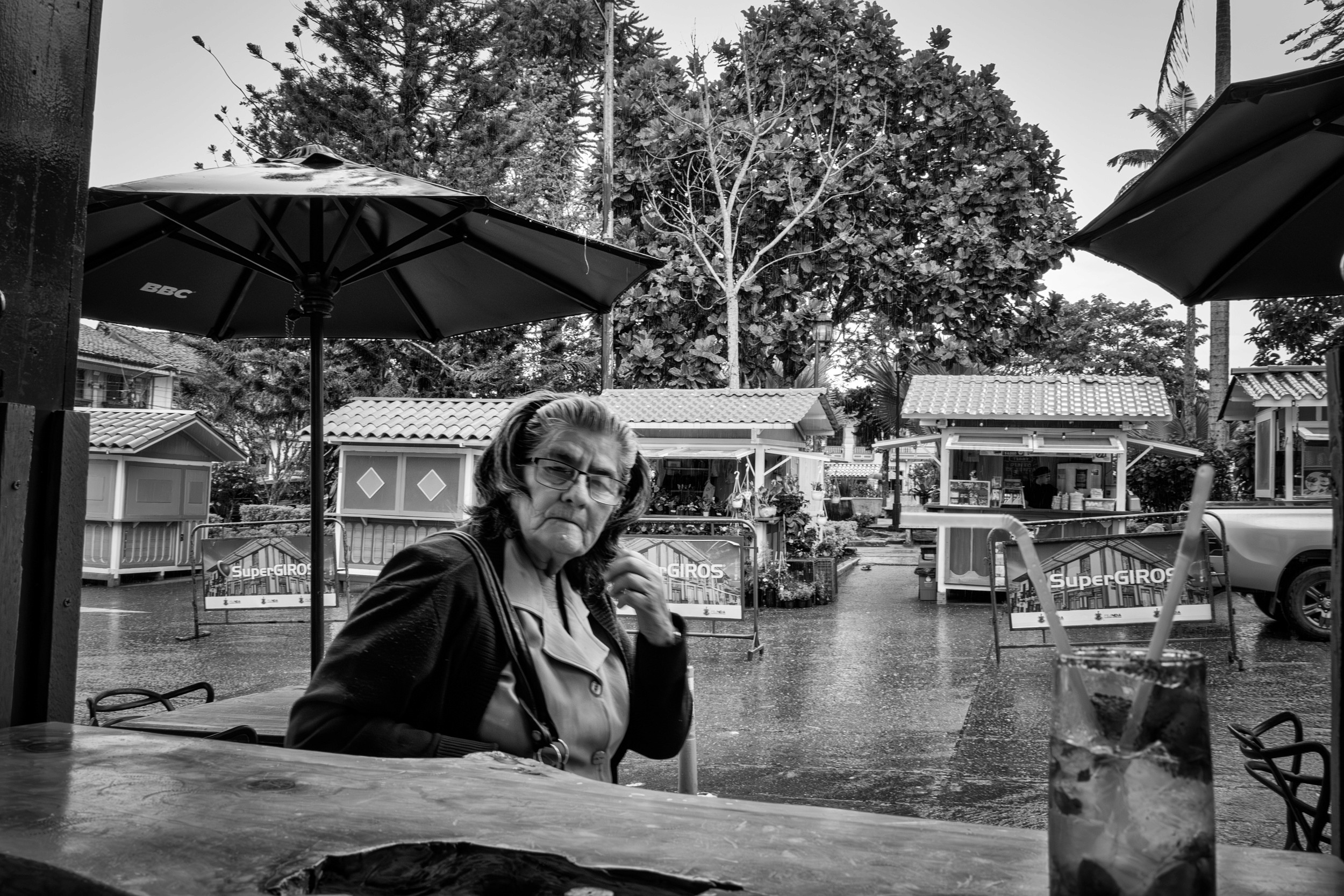 Rainy street scene with people passing by a bar window.