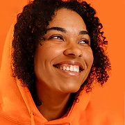 Smiling person with curly hair wearing an orange hoodie against a bright orange background.