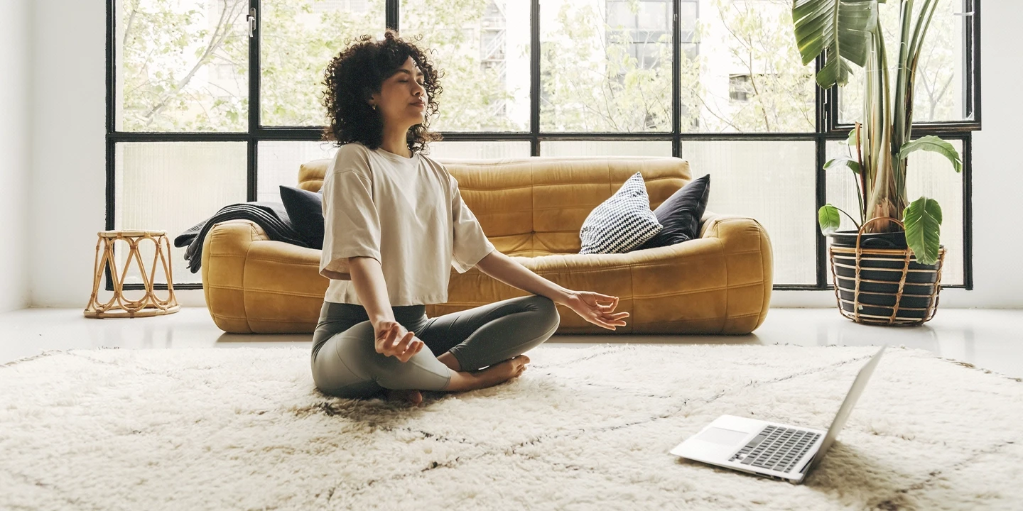 Pessoa meditando de frente para um laptop, representando um benefício corporativo voltado para a saúde mental