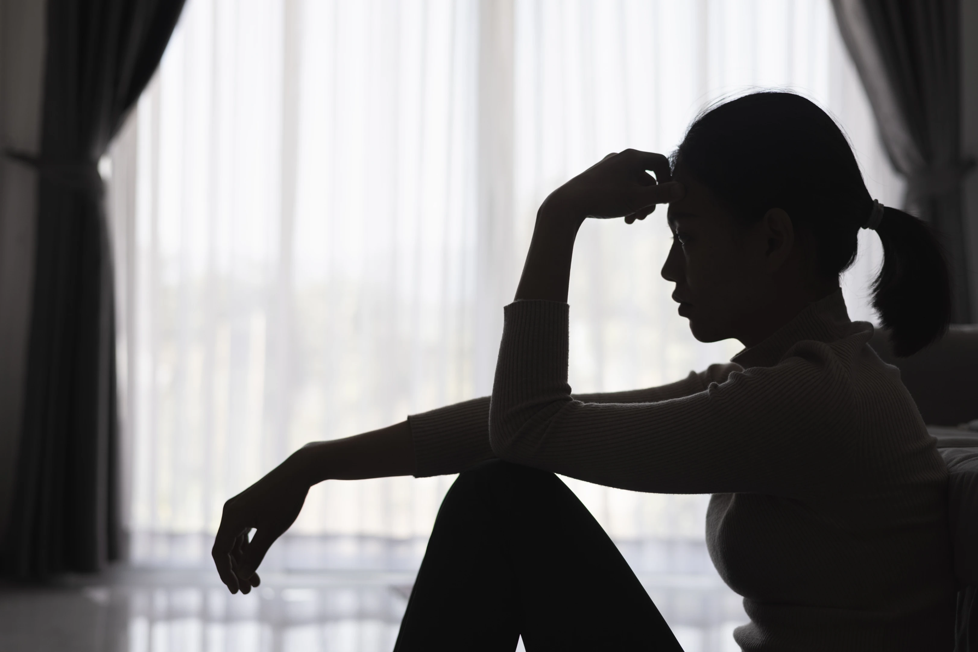 Teen sitting by a window looking discouraged while a parent offers supportive conversation.