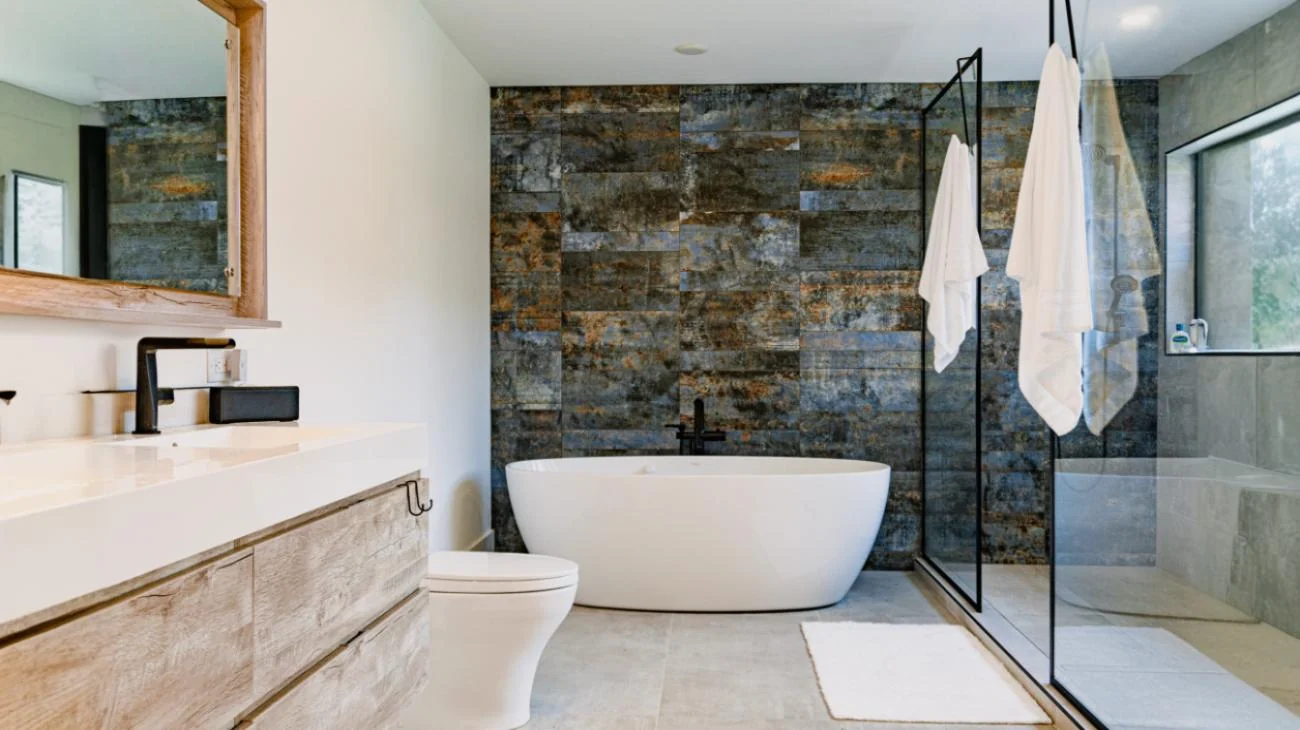Spa-inspired luxury bathroom with freestanding soaking tub, textured stone feature wall, frameless glass shower, and custom vanity in Vancouver custom home