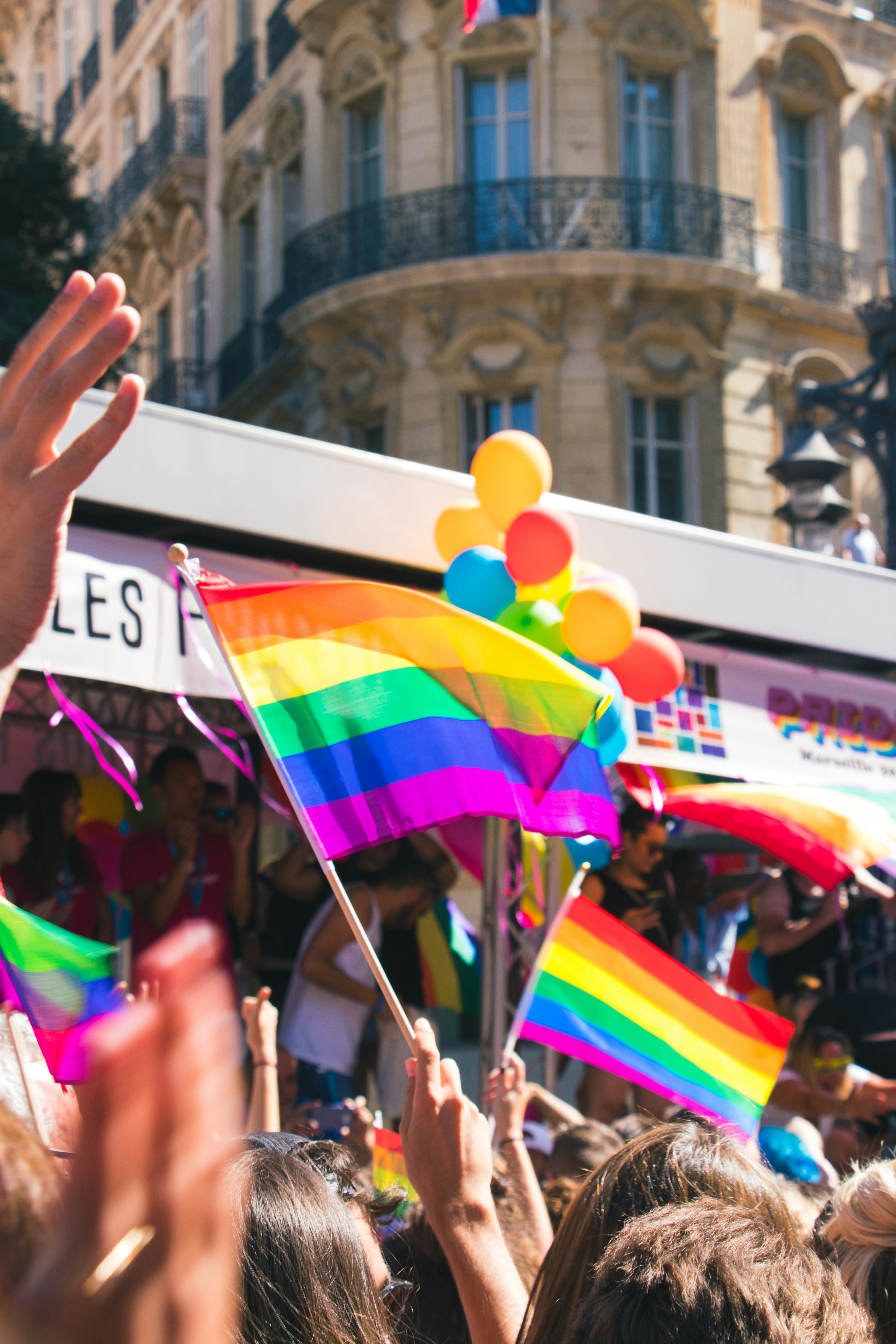Een menigte op een pride-parade houdt elkaars hand vast in een viering, met een kleurrijke regenboogvlag die duidelijk zichtbaar is.