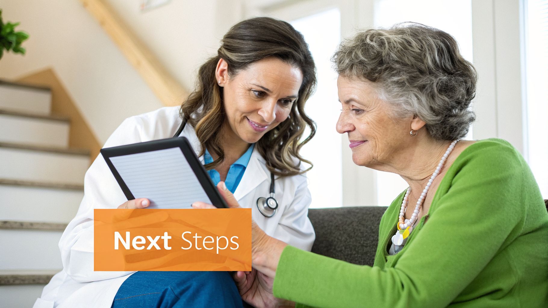 A smiling female doctor in a white coat shows a tablet to an elderly female patient.