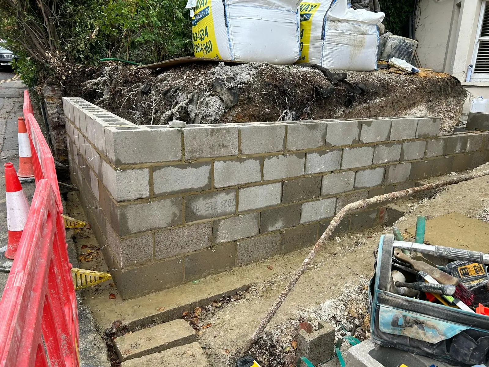 A partially constructed wall made of cinder blocks, with construction materials and tools scattered nearby.
