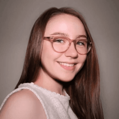 Portrait of Emily Gambino-Walker smiling while wearing glasses and a light-colored top against a neutral background.