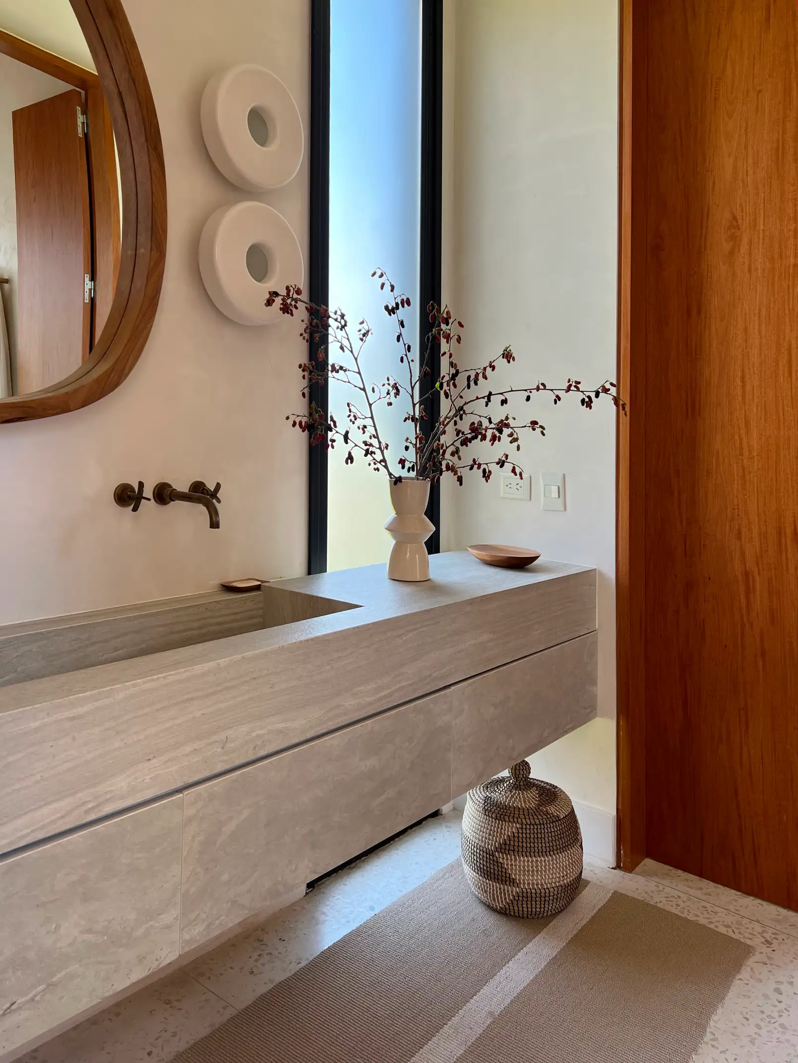 Baño minimalista con lavamanos de piedra y arreglo botánico para proyectos residenciales que integran naturaleza y materiales nobles.