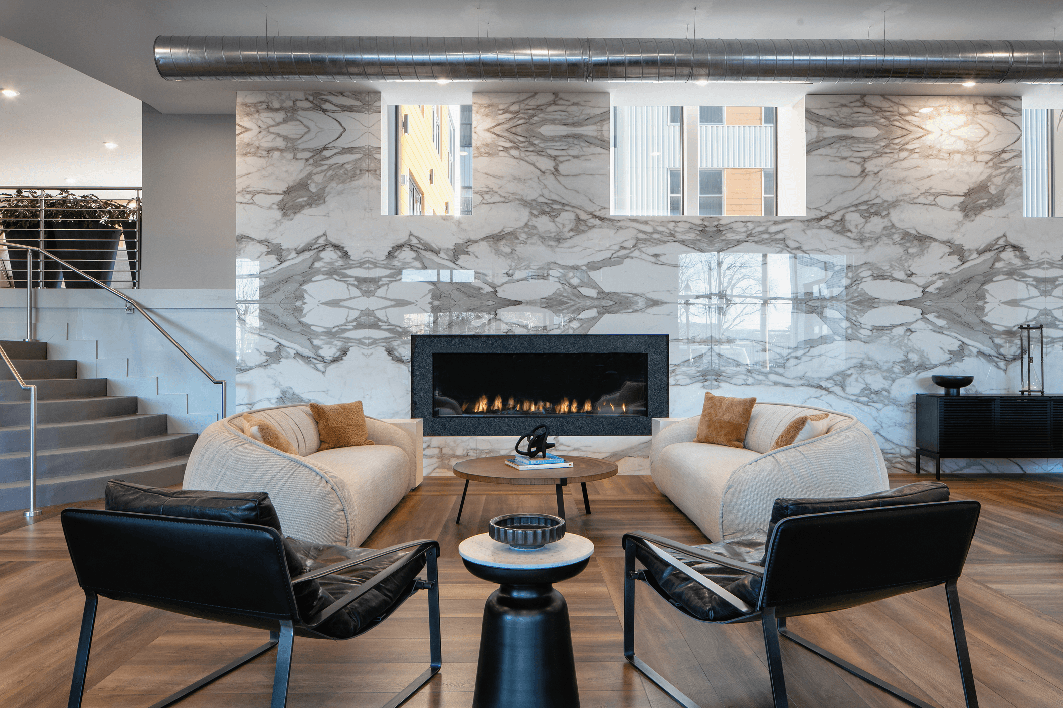 Modern lounge area featuring two white armchairs, black chairs, and a stylish fireplace against a decorative wall.