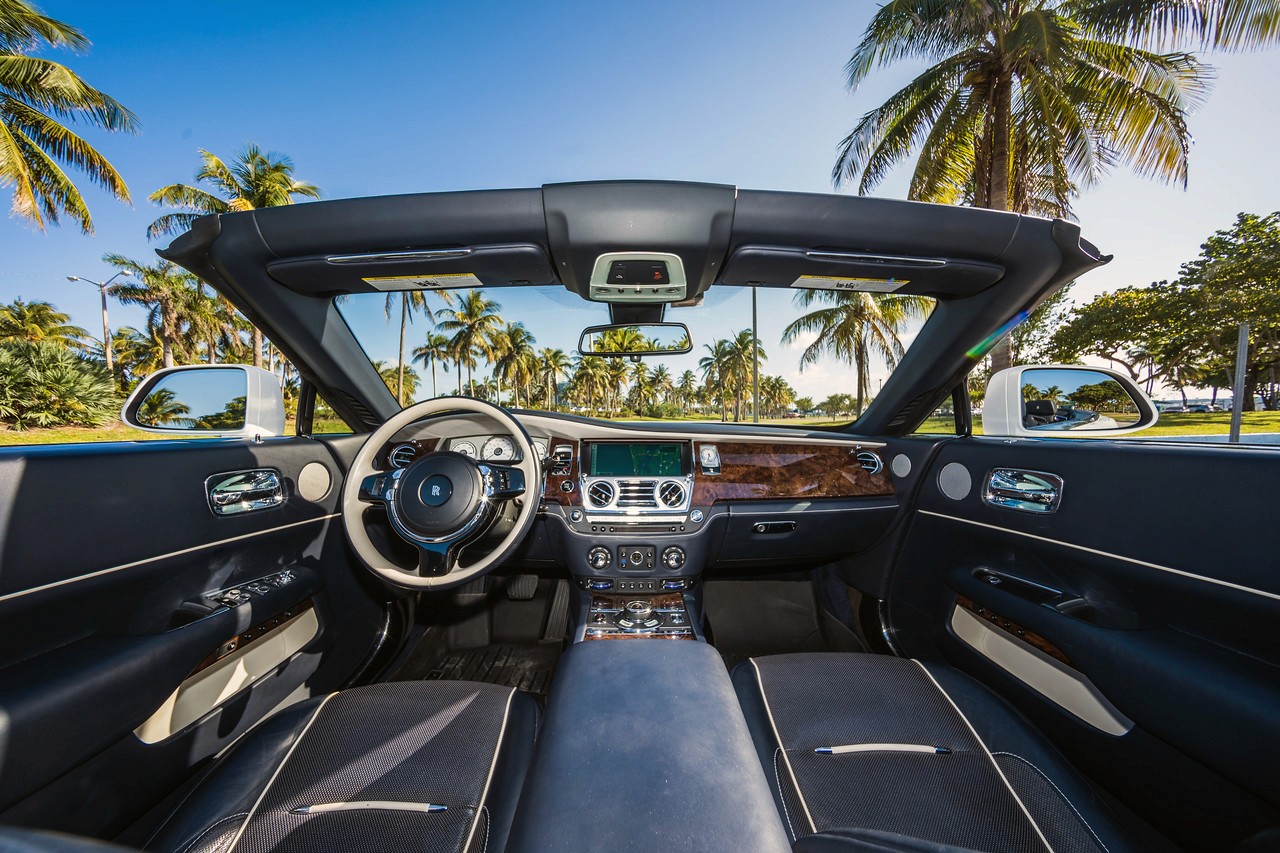 Interior dashboard view of the Rolls-Royce Dawn, highlighting the luxury steering wheel, infotainment system, and premium materials.