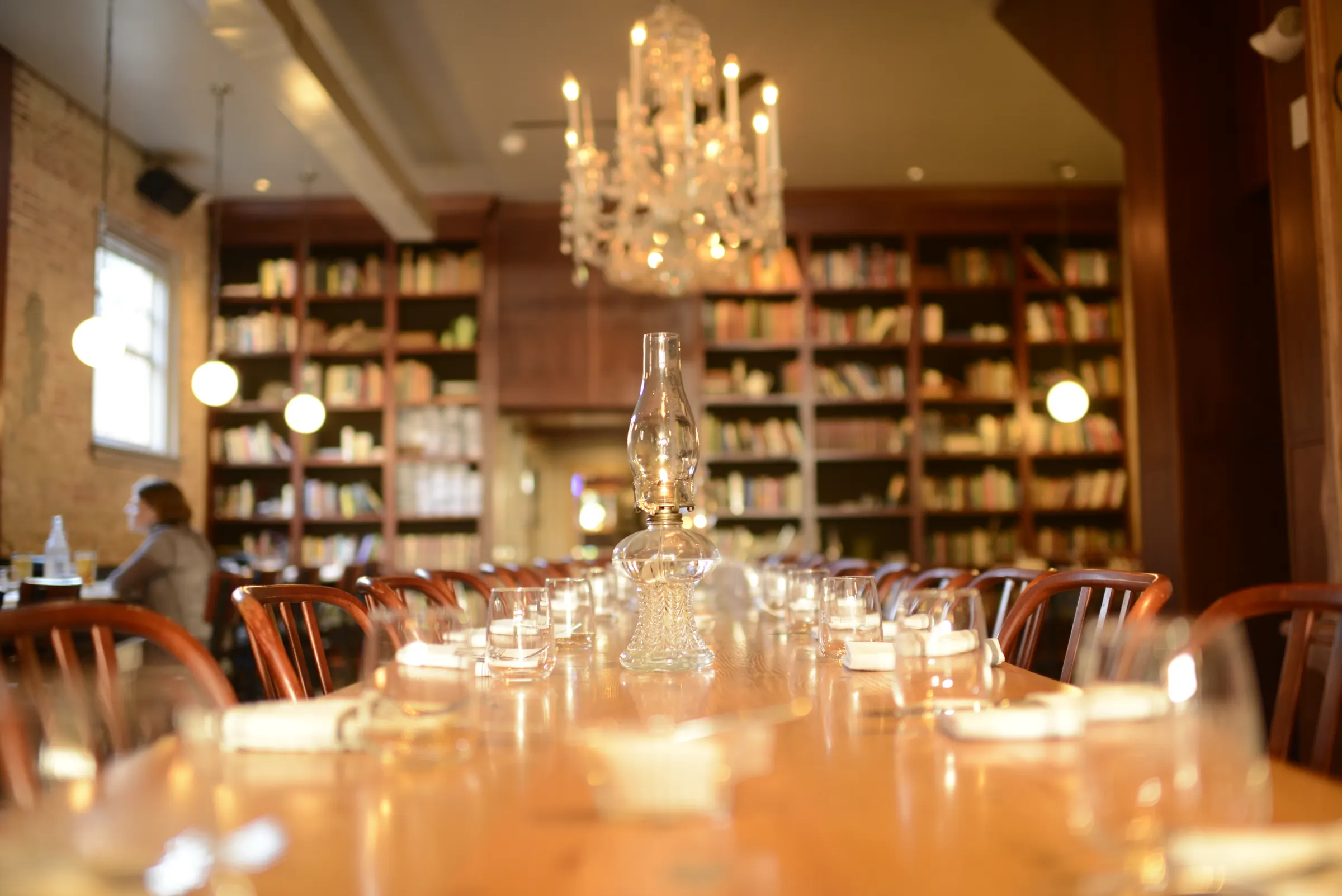 Long community table set under a chandelier with bookshelves at Asterisk