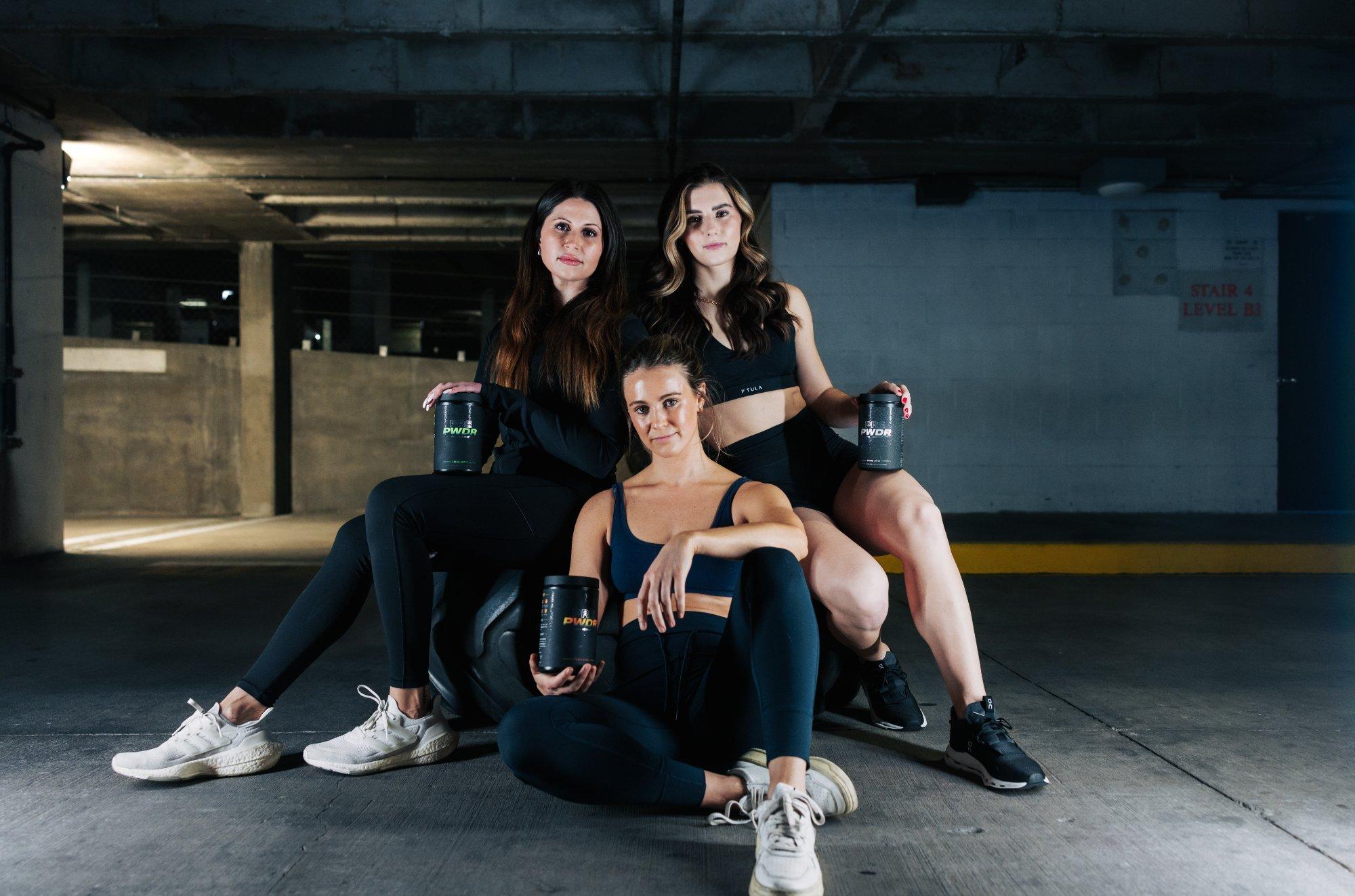 Three women dressed in athletic clothing each holding a cup