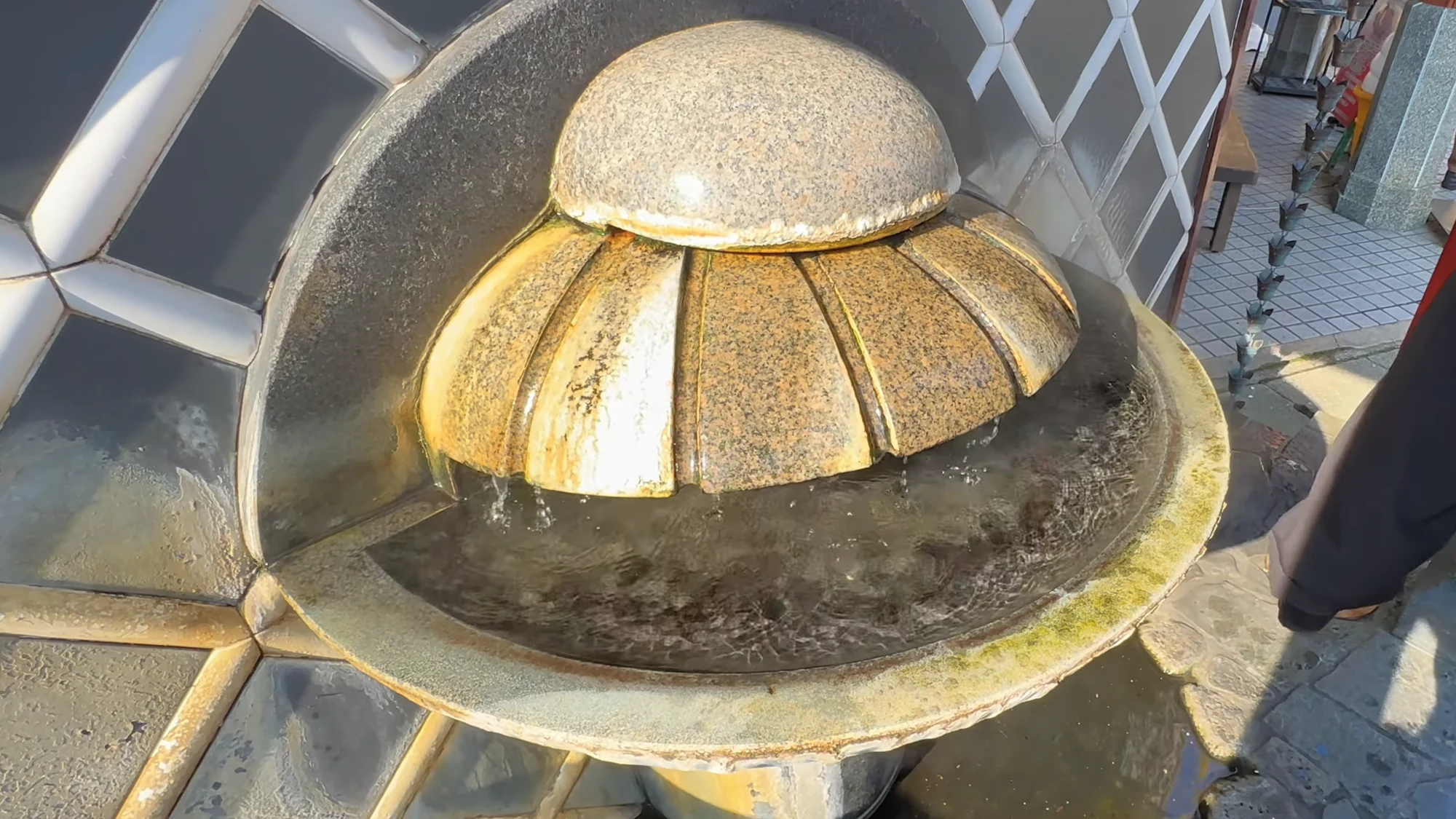 Close view of a carved stone drinking basin with hot spring water running over its fluted dome.