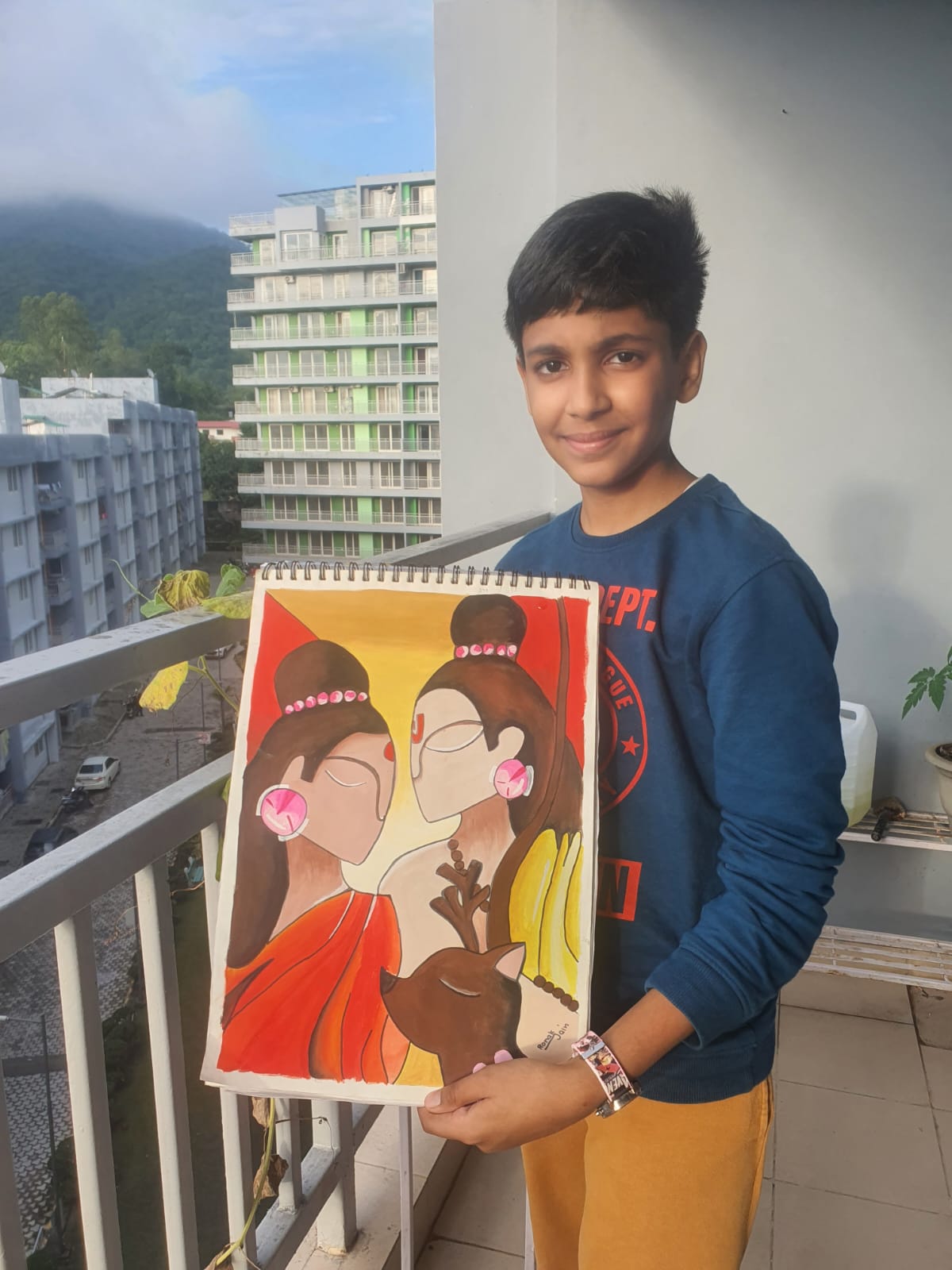 A boy stands on a balcony holding a colorful painting of Ram and Sita from the Hindu religion in the Creative Pod studio.