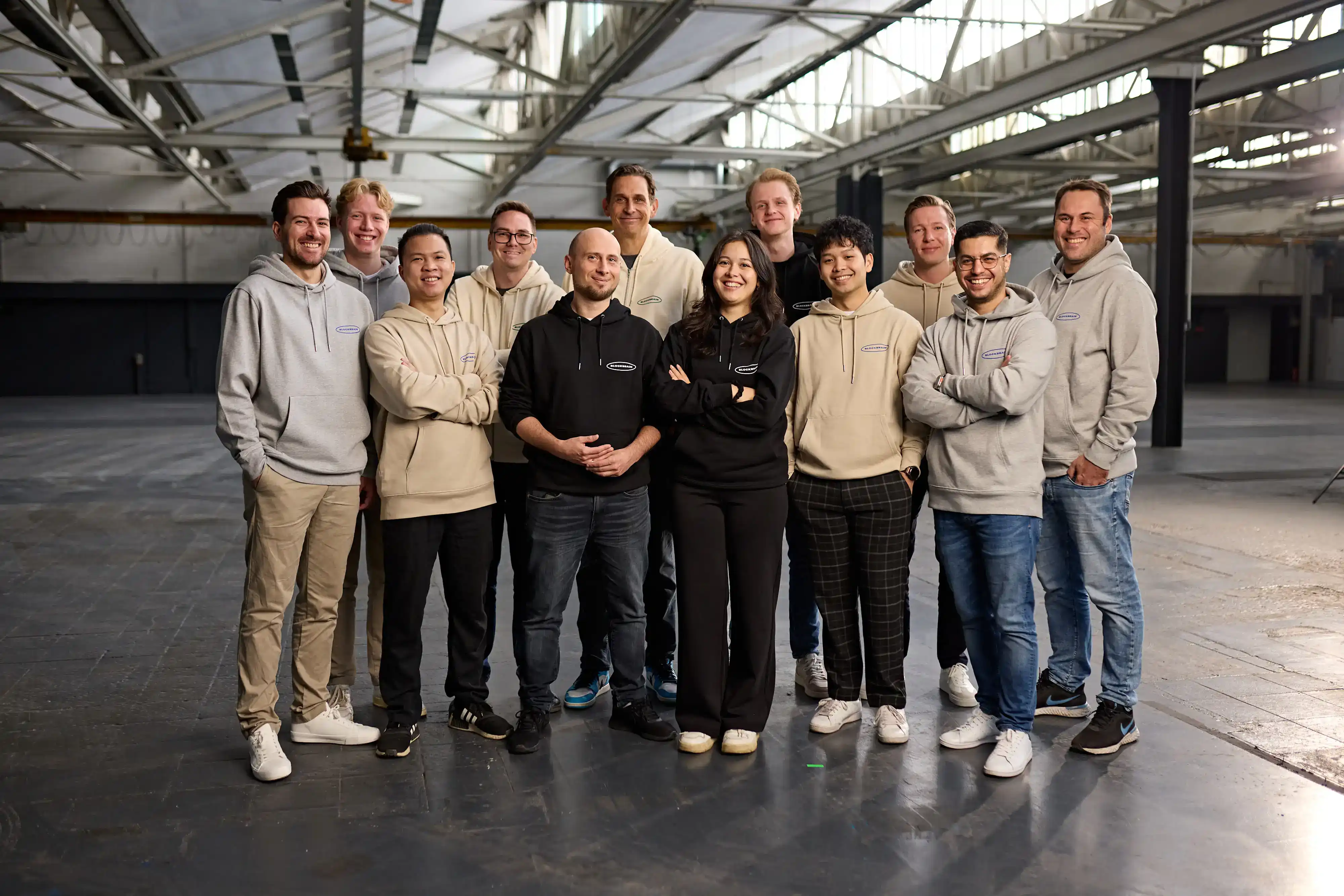 Team members posing together in a spacious industrial warehouse, all wearing branded hoodies