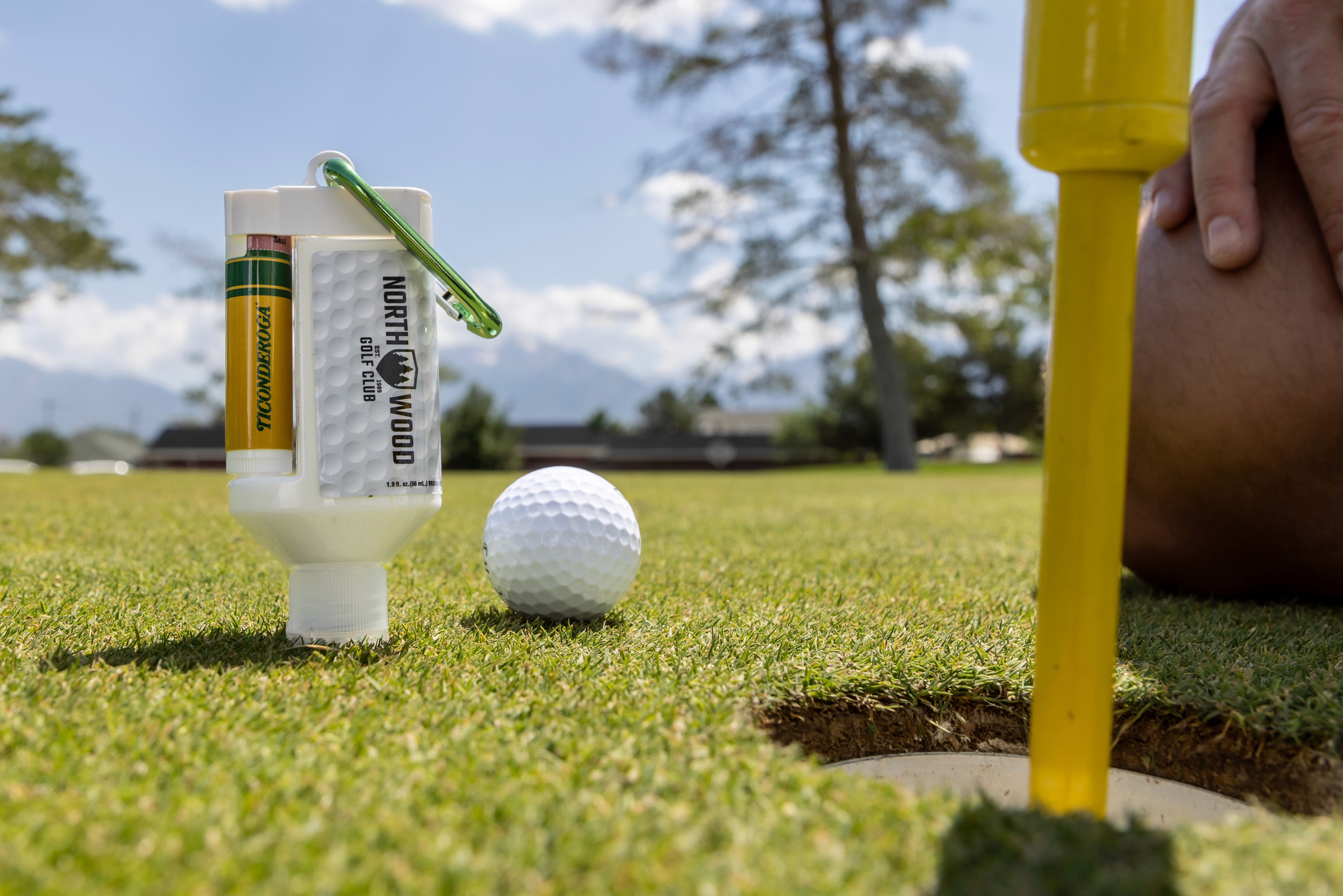 The Duo Bottle on golfing green next to a person kneeling down next to the hole near the golf ball.