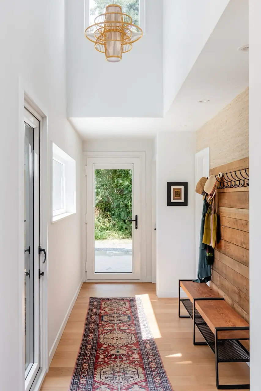 Modern two-story home with large glass windows, warmly lit interiors, and a balcony. Surrounded by trees and a manicured lawn at dusk. Cozy ambiance.