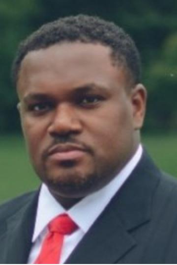 Portrait of a Black man in a suit and red tie looking at the camera.