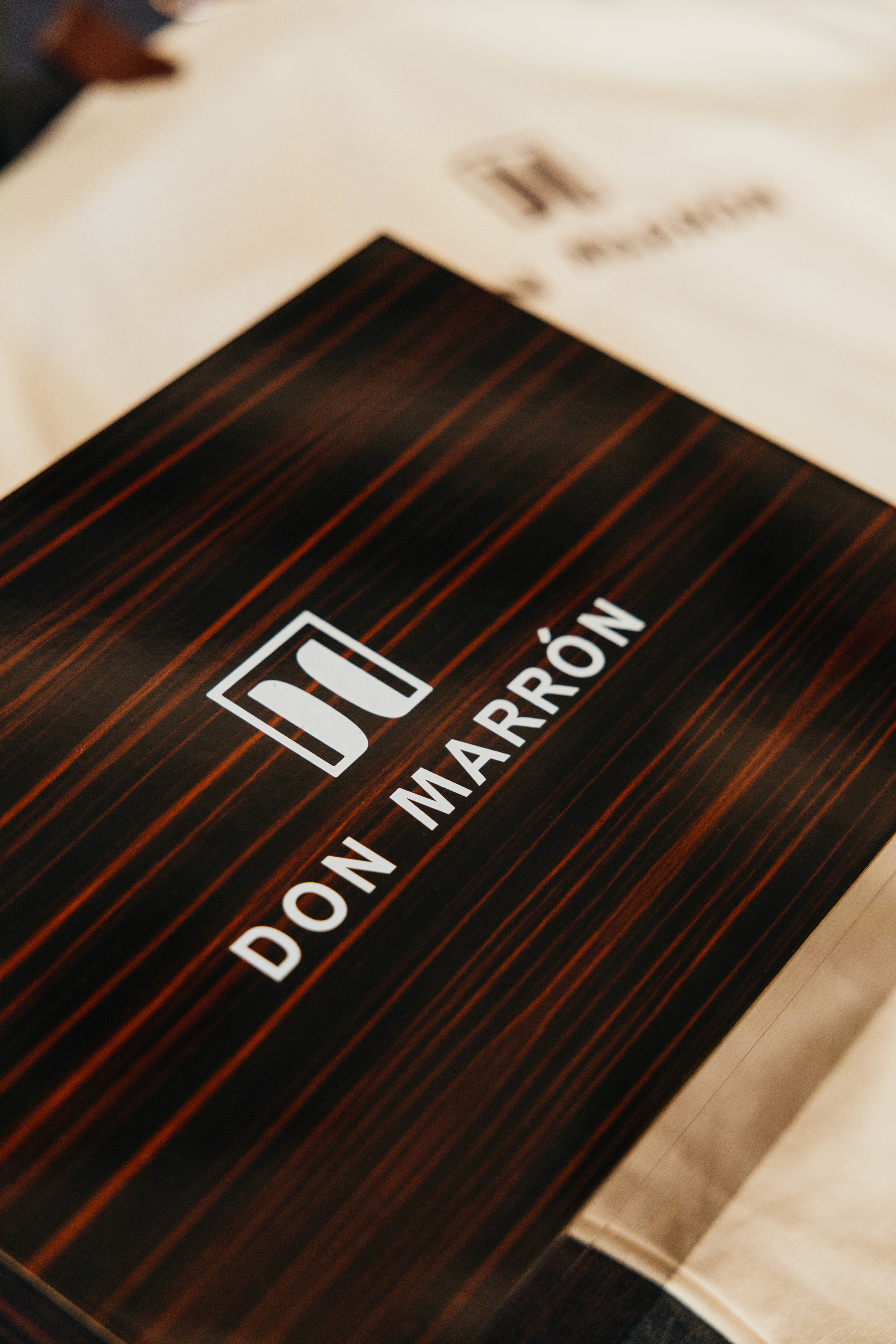 Don Marrón member leaning against a yellow Italian wall in a mustard shirt and tailored blue trousers, holding a Don Marrón garment bag. A modern expression of effortless style and luxury craftsmanship.