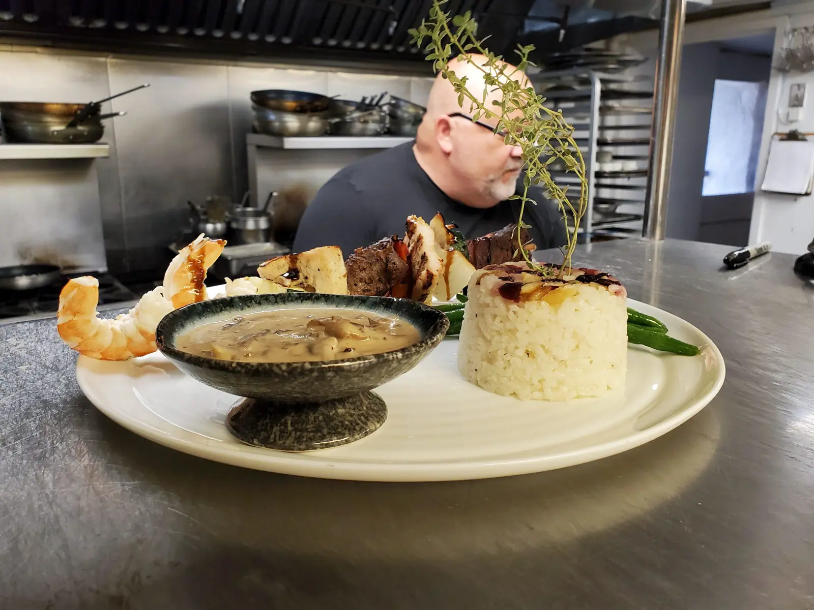 Plated surf and turf meal with shrimp, steak, rice, and mushroom sauce.