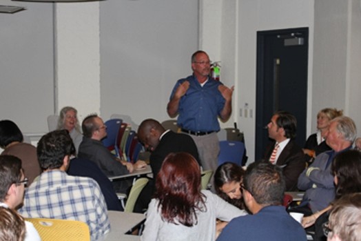 A man giving a speech in a room full of people