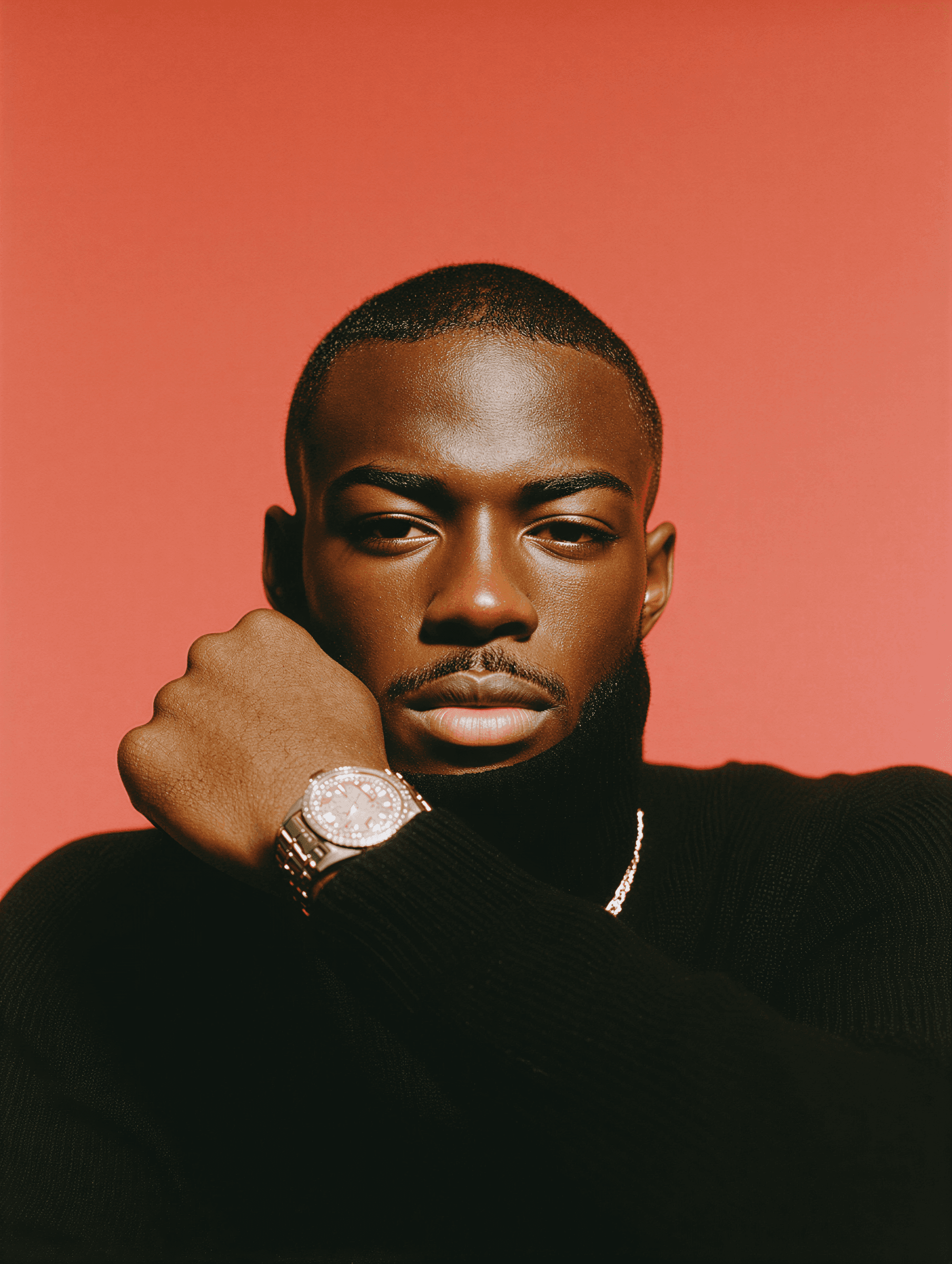 A man in a black shirt poses against a red background, showcasing a watch on his wrist with a confident expression.