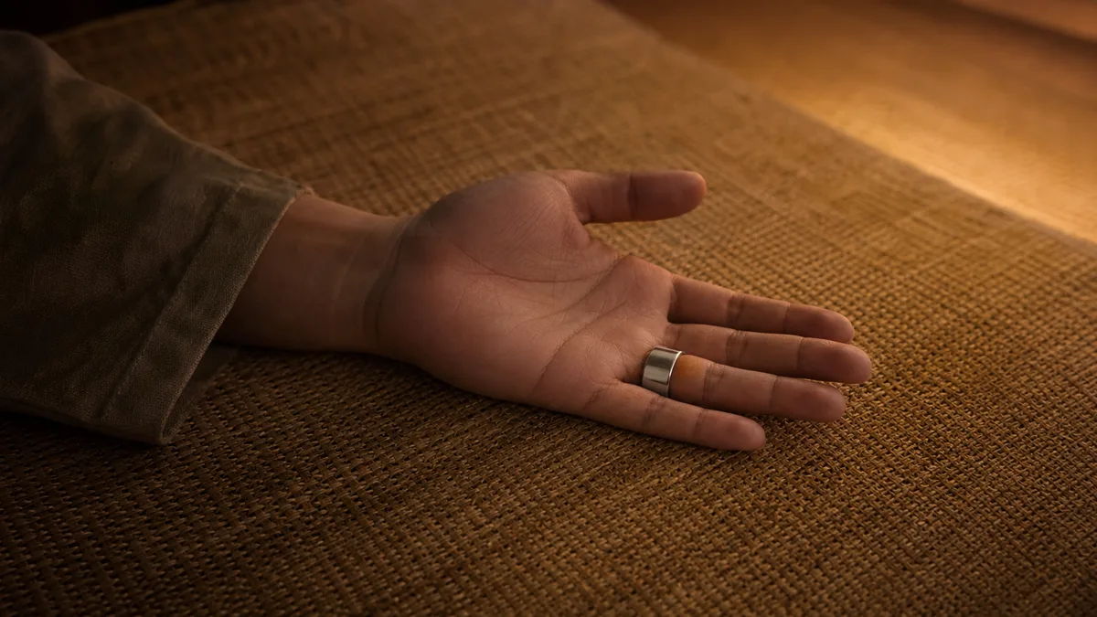 Open hand wearing a silver smart tasbih ring resting on a warm woven prayer mat