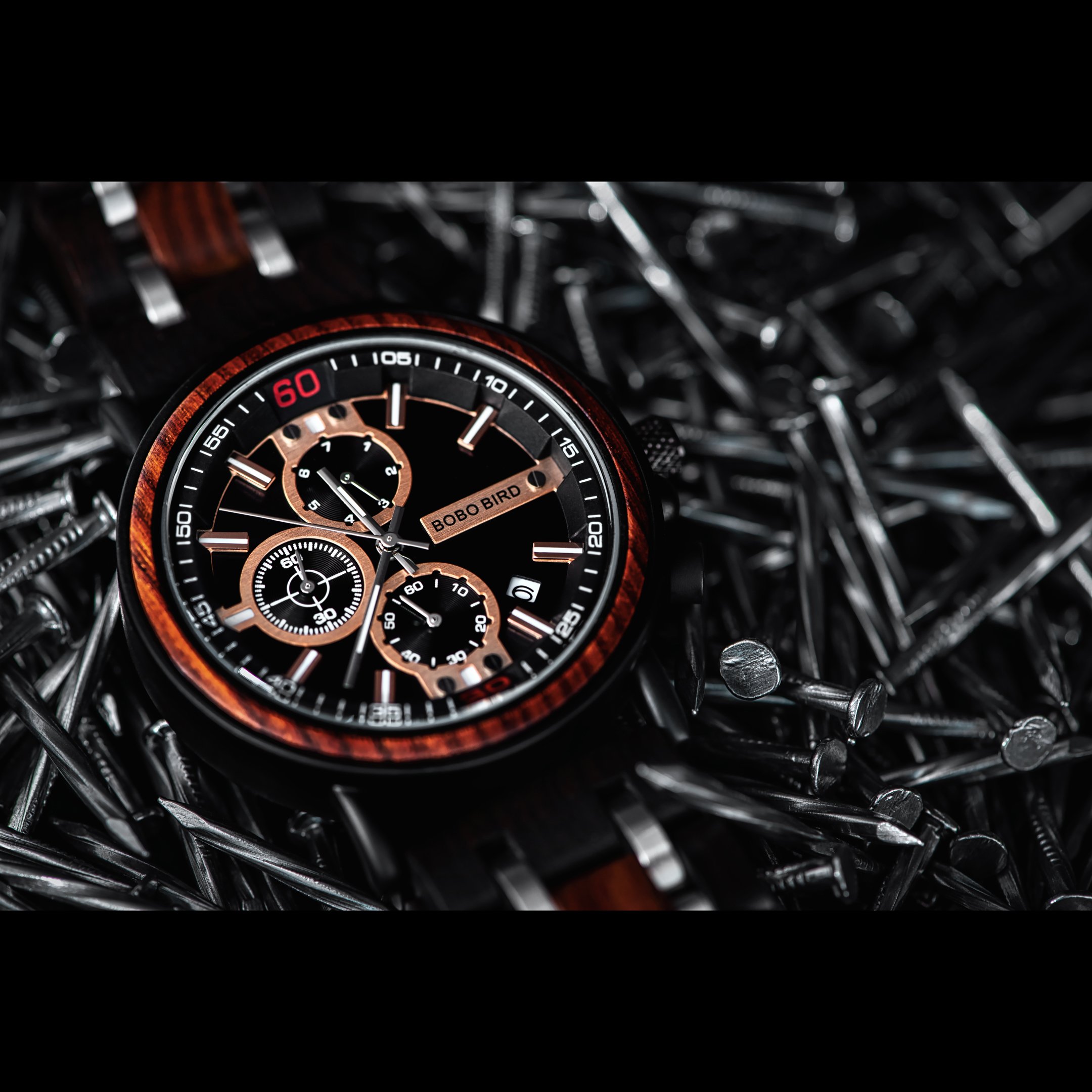 Commercial product photography featuring a Bobo Bird wristwatch with cherry wood accents displayed on a bed of steel nails to emphasize durability and craftsmanship.
