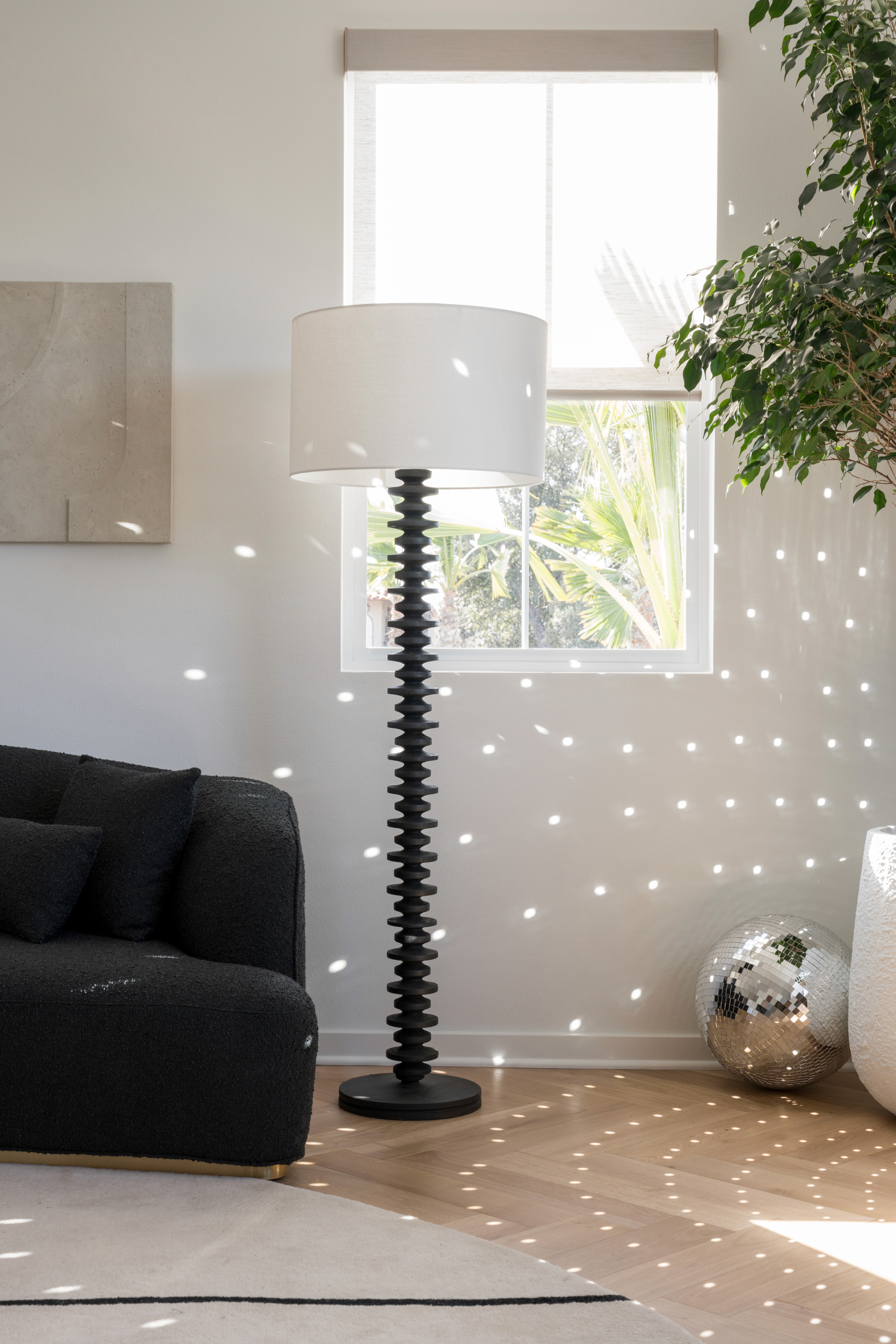 Floor lamp with black metal base and white shade, decorative disco balls displayed on floor reflecting on living area