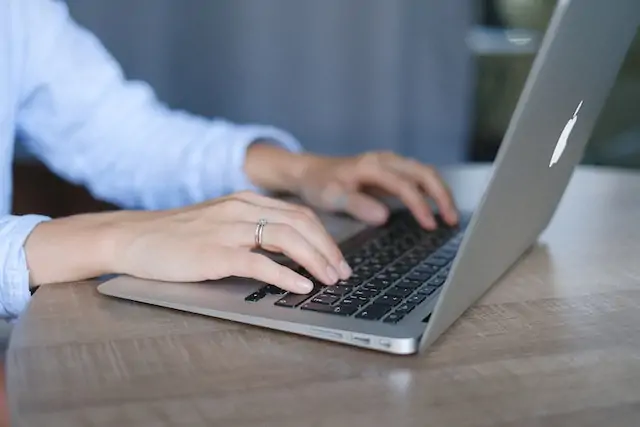 person in blue shirt writing on their laptop at a desk